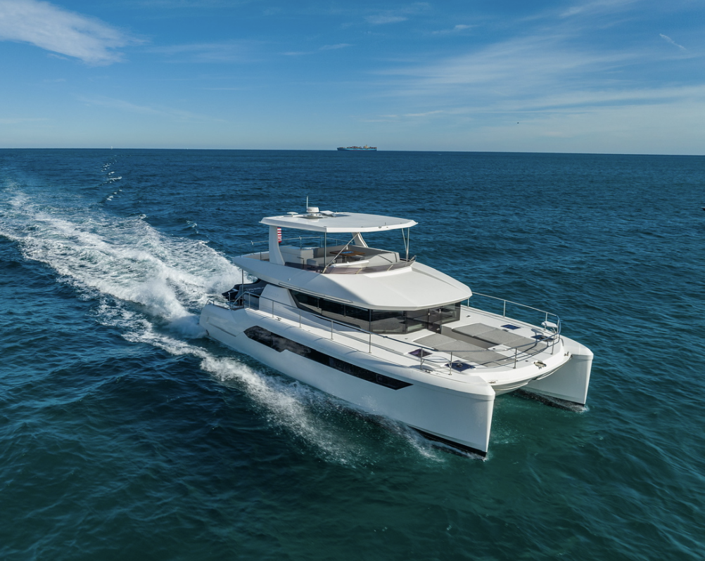 Luxury white yacht sailing on deep blue ocean with clear sky and a distant cargo ship in the background.