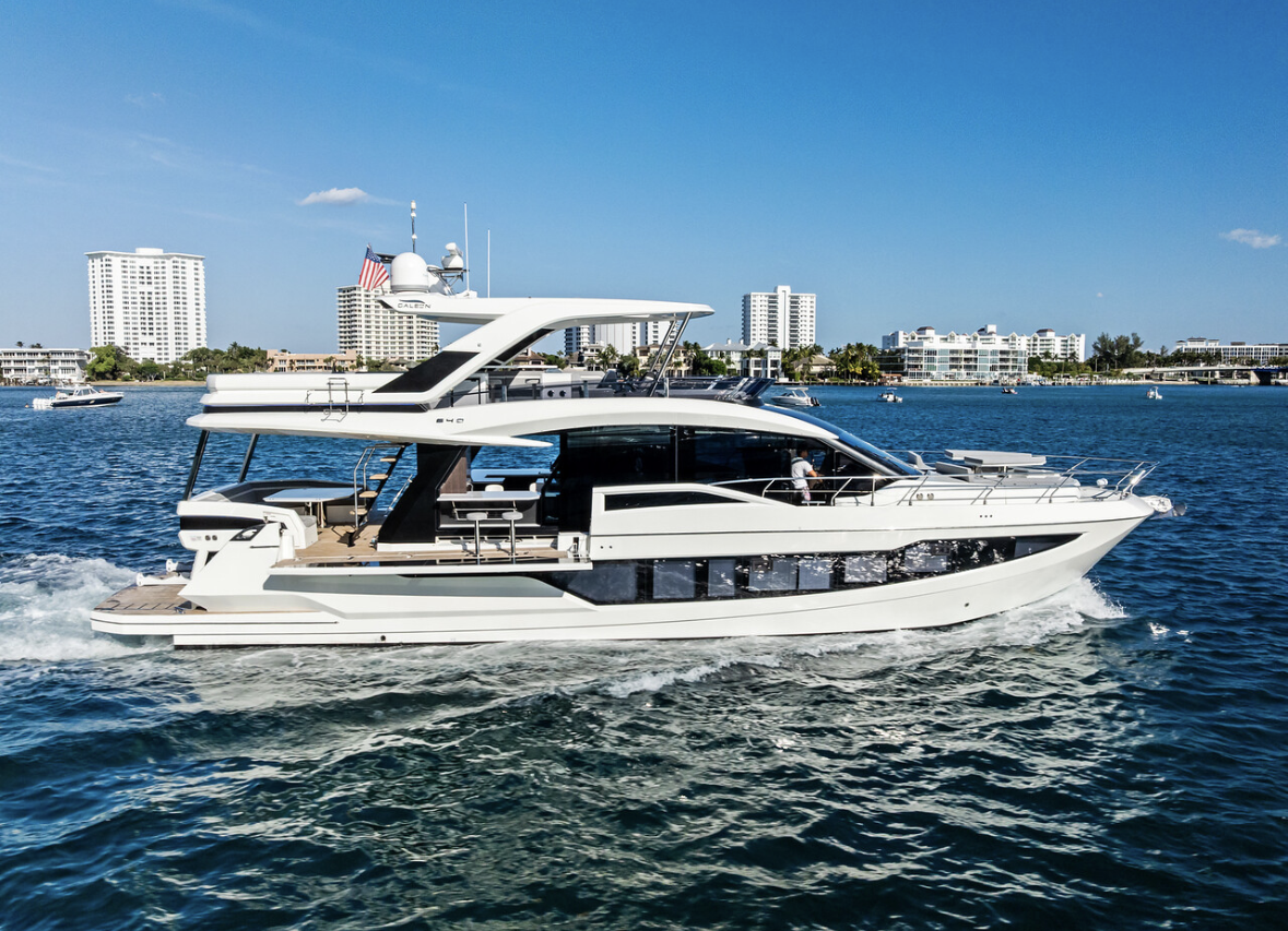 White yacht cruising on blue water with waterfront buildings in background on sunny day.