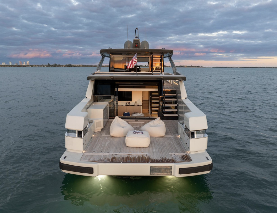A luxury yacht floating on calm water with a city skyline in the distance, during sunset or sunrise.
