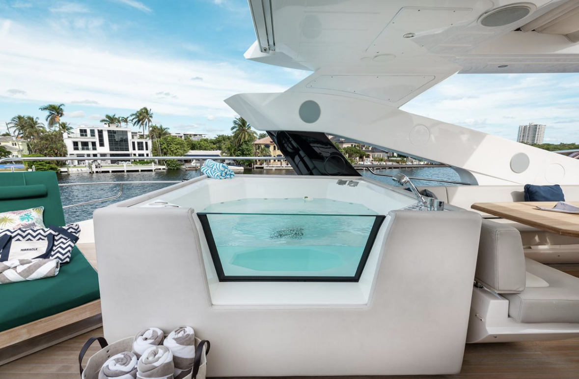 Luxury yacht with a built-in hot tub on deck, overlooking water and modern homes in the background.