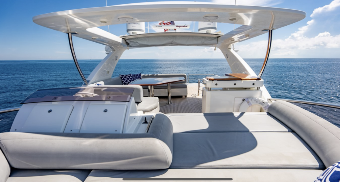 Luxury yacht on open ocean with seating area, table, and shade canopy under blue sky