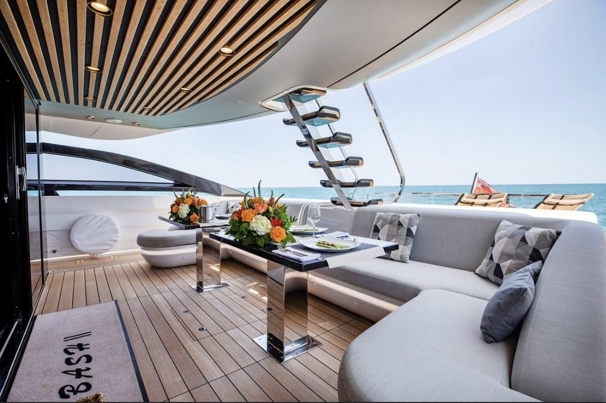 Luxurious yacht deck with dining table, floral arrangements, and seating area, overlooking the ocean under a clear sky.
