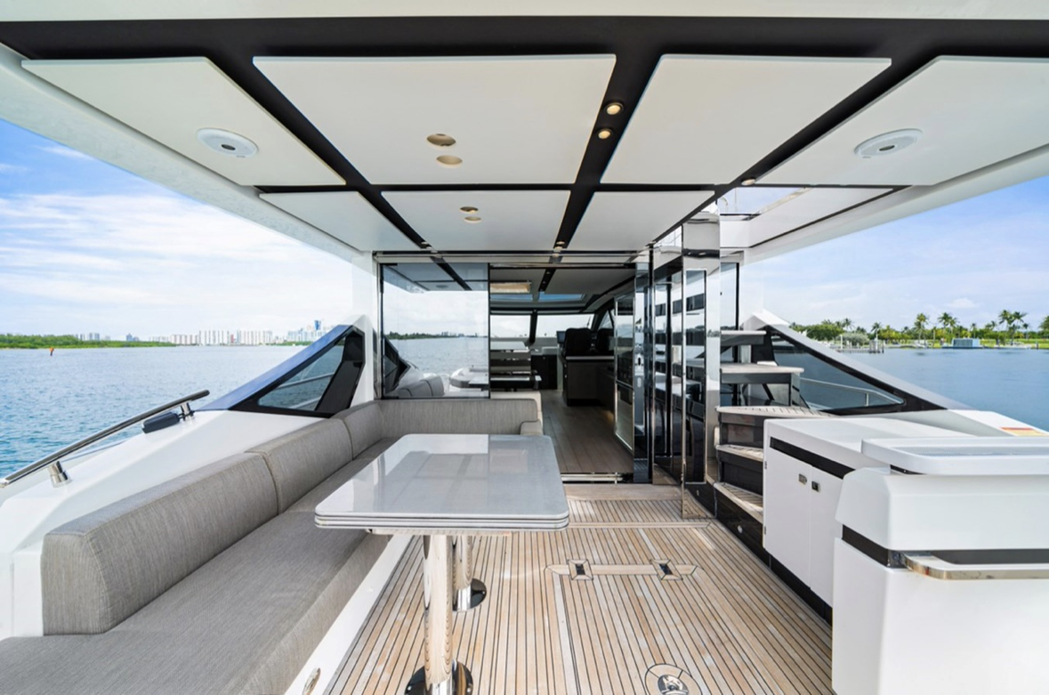 Luxury yacht deck with seating, table, and outdoor kitchen, overlooking water and city skyline in the distance.