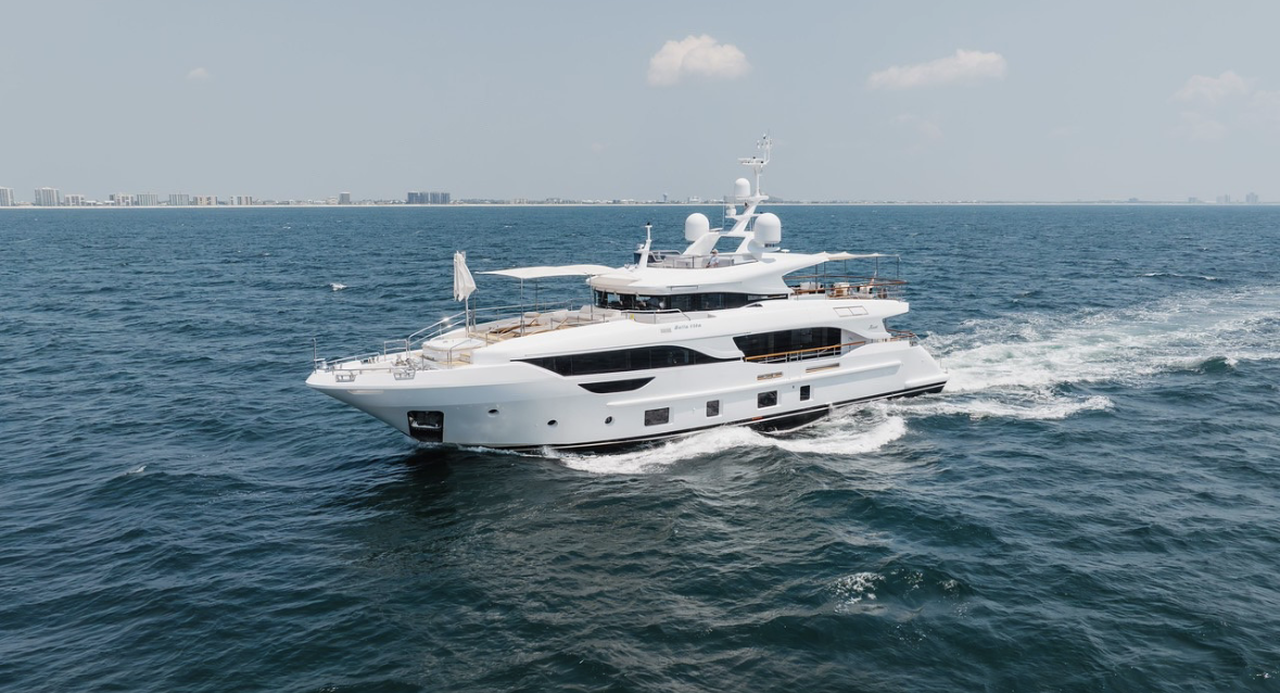 A large white yacht cruising on the ocean with a city skyline in the background.