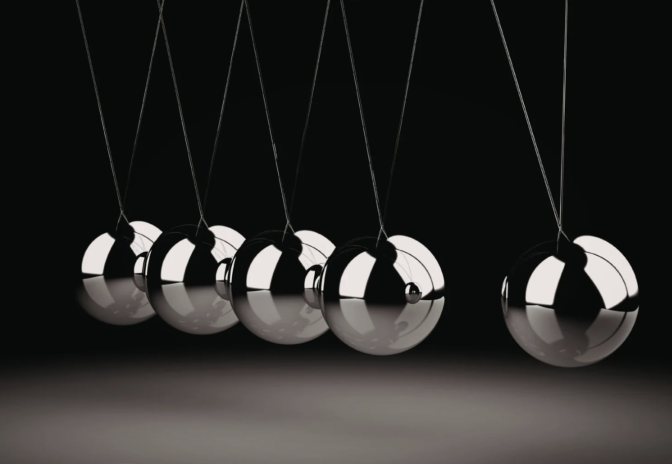 A Newton's Cradle with five shiny metal balls suspended by thin wires against a black background.
