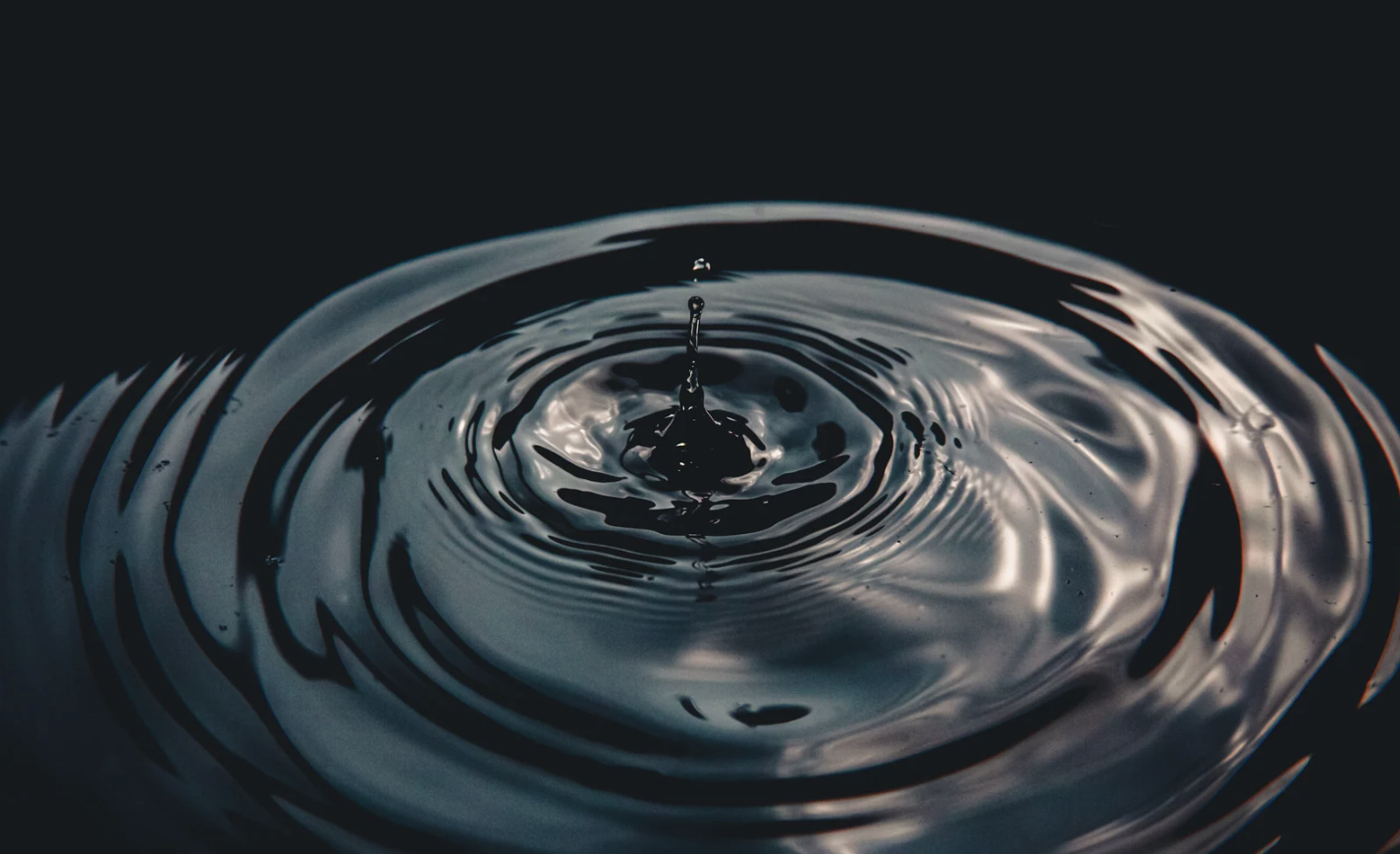 Close-up of a water droplet creating ripples on a dark surface.