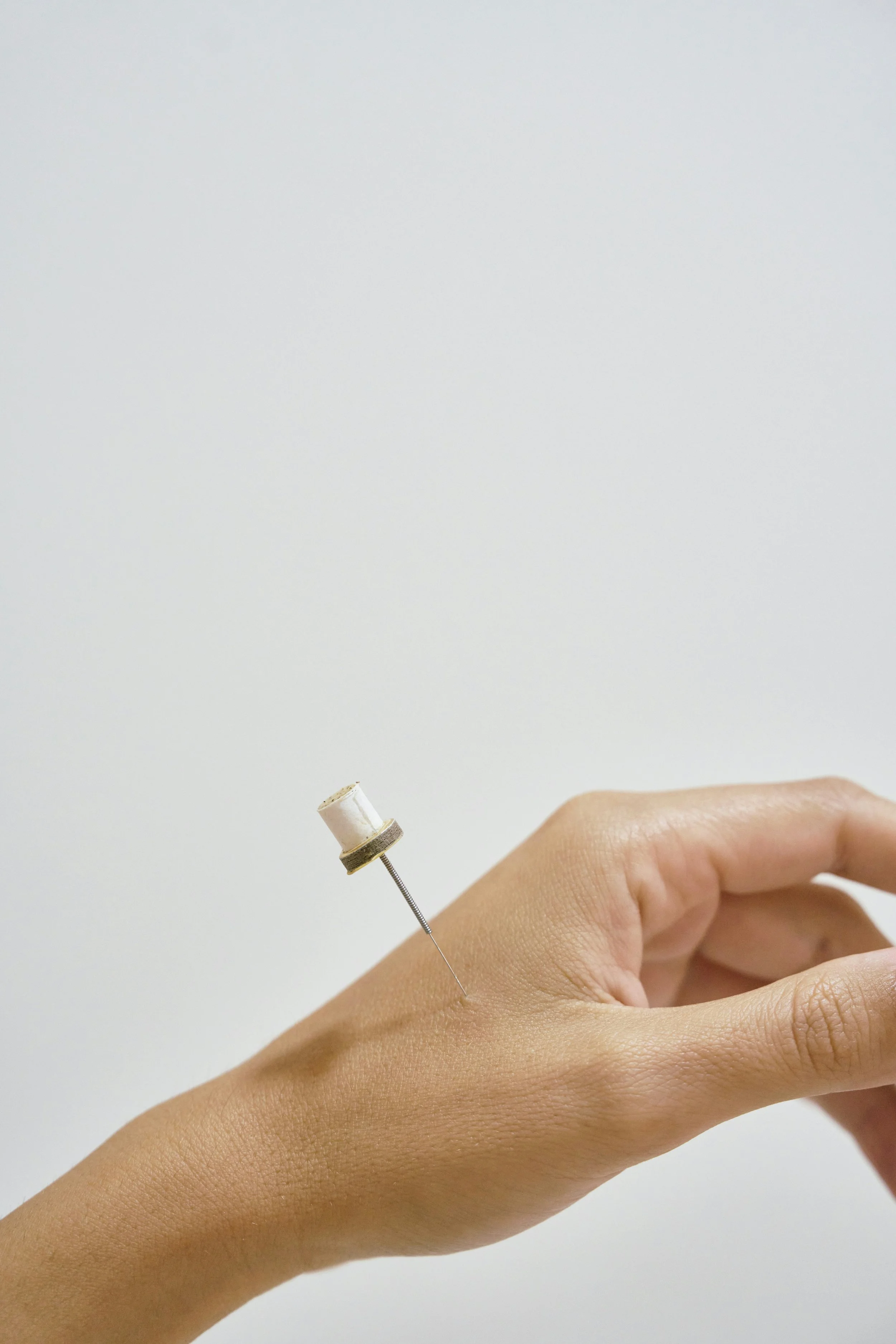 A person's hand with a small medical vaccine or injection needle inserted into the back of the hand.