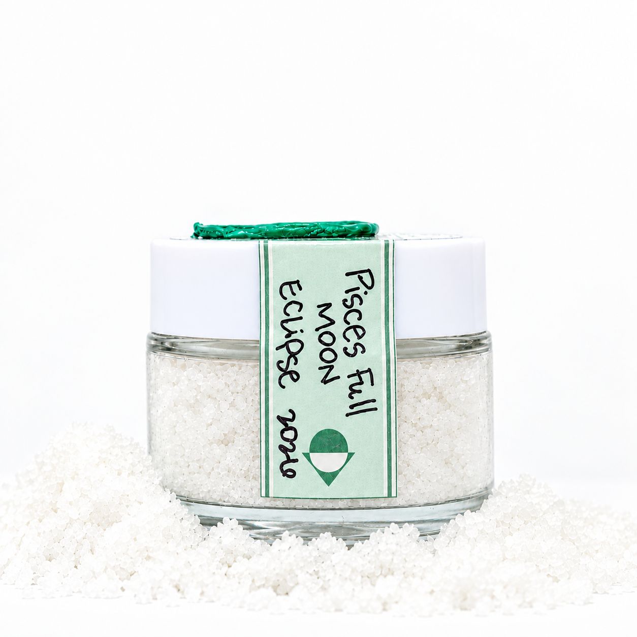 A glass jar with a white lid labeled 'Pisces full moon 2026' sitting on a white surface surrounded by scattered white sacred salt, against a plain white background.