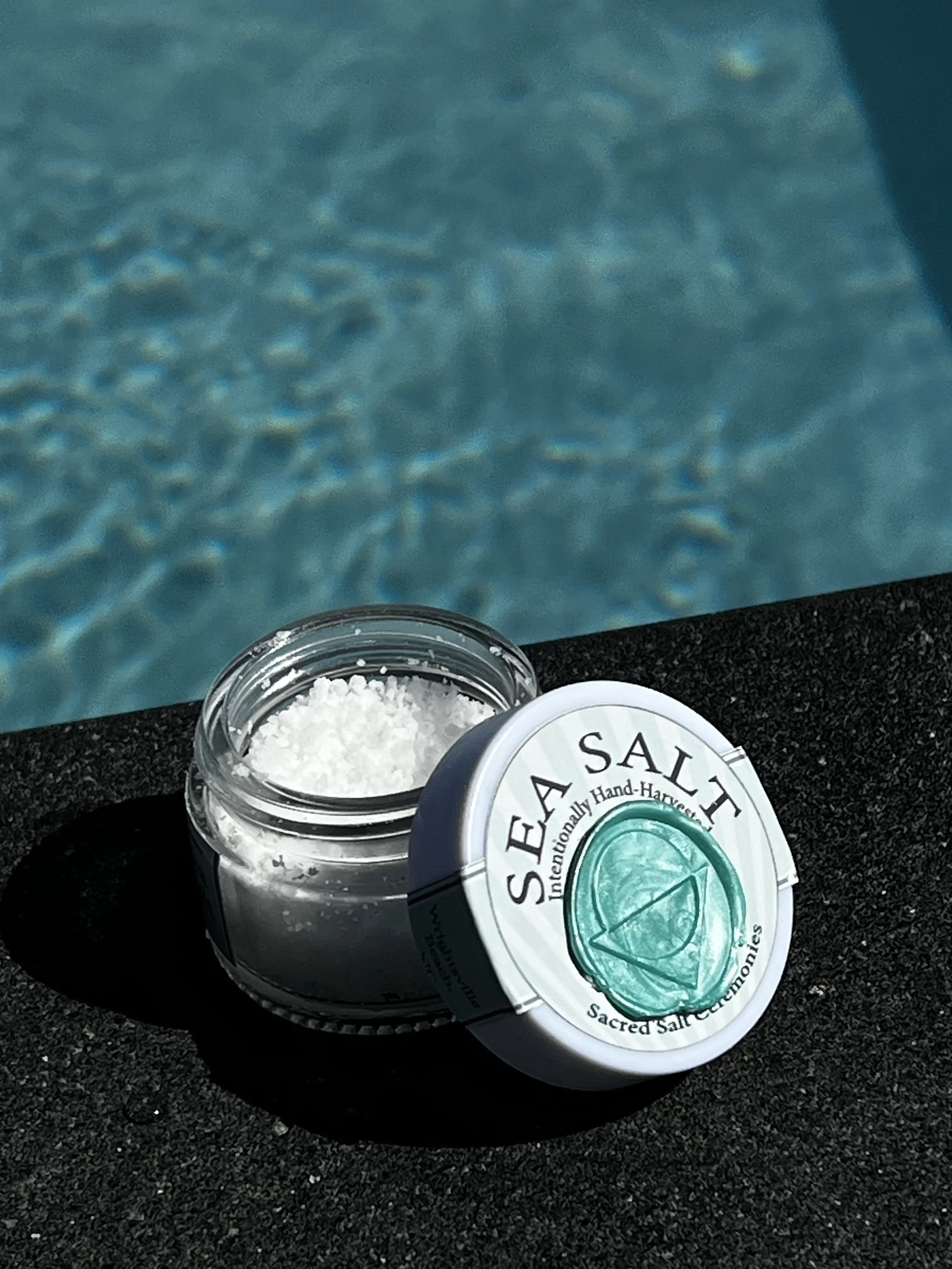 Open container of Sacred Salt, a salt product, on a black textured surface with a blue textured background.
