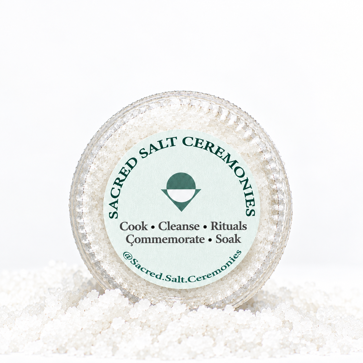 A jar of sacred salt from Sacred Salt Ceremonies, surrounded by salt crystals, with a label indicating it is used for cooking, cleansing, rituals, commemorations, and soaking.