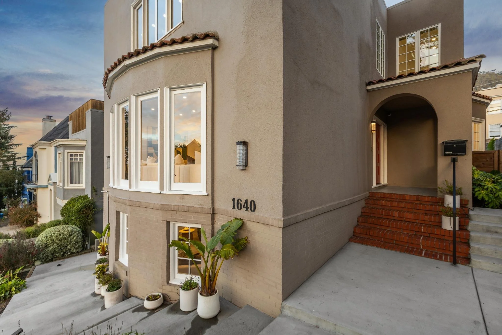 Exterior view of a multi-story beige house with white trim, brick steps, and several potted plants near the entrance, displaying house number 1640.
