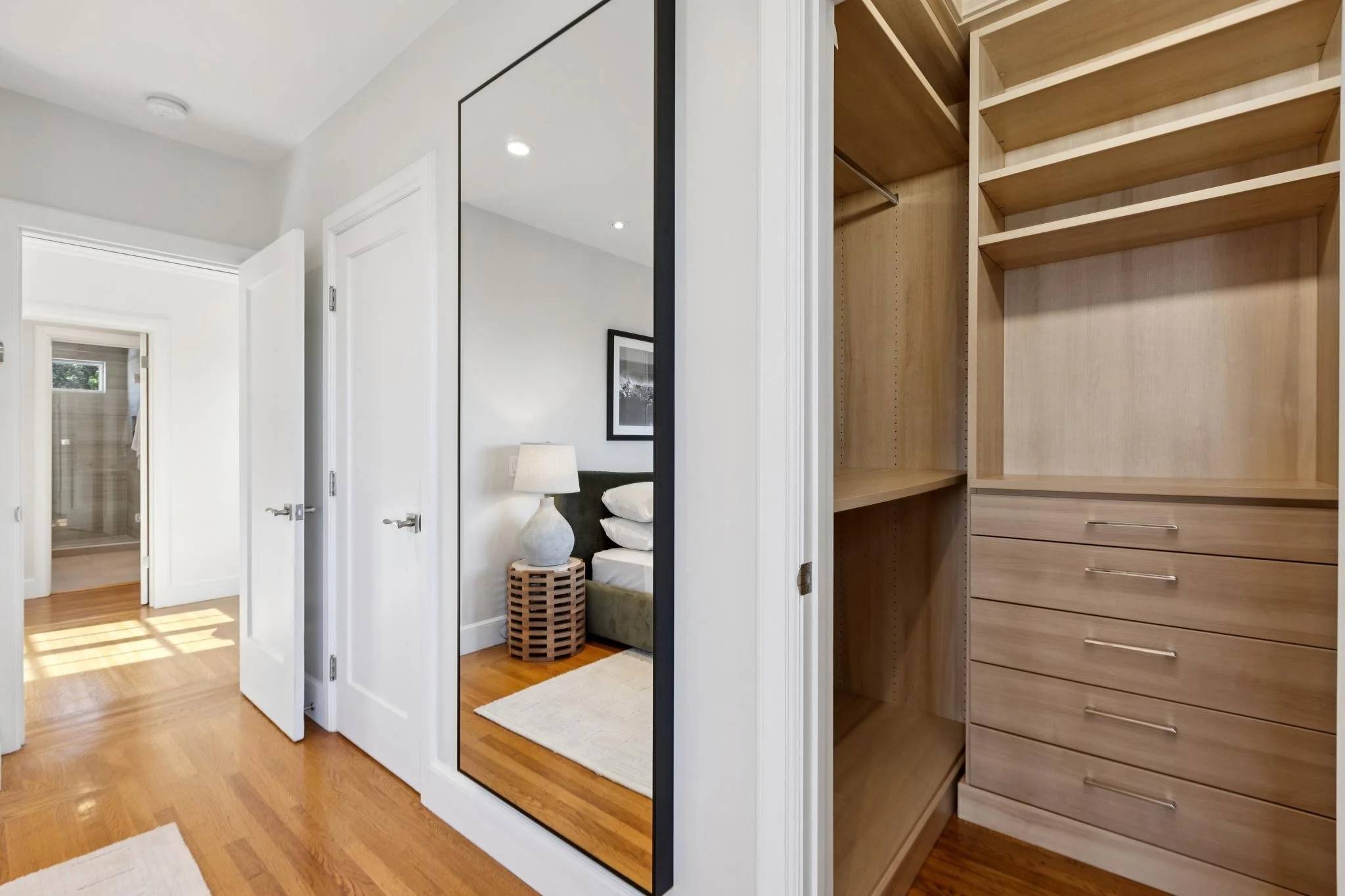 View of a bedroom with a closet, a standing mirror, and a bedside table with a lamp in a modern home.