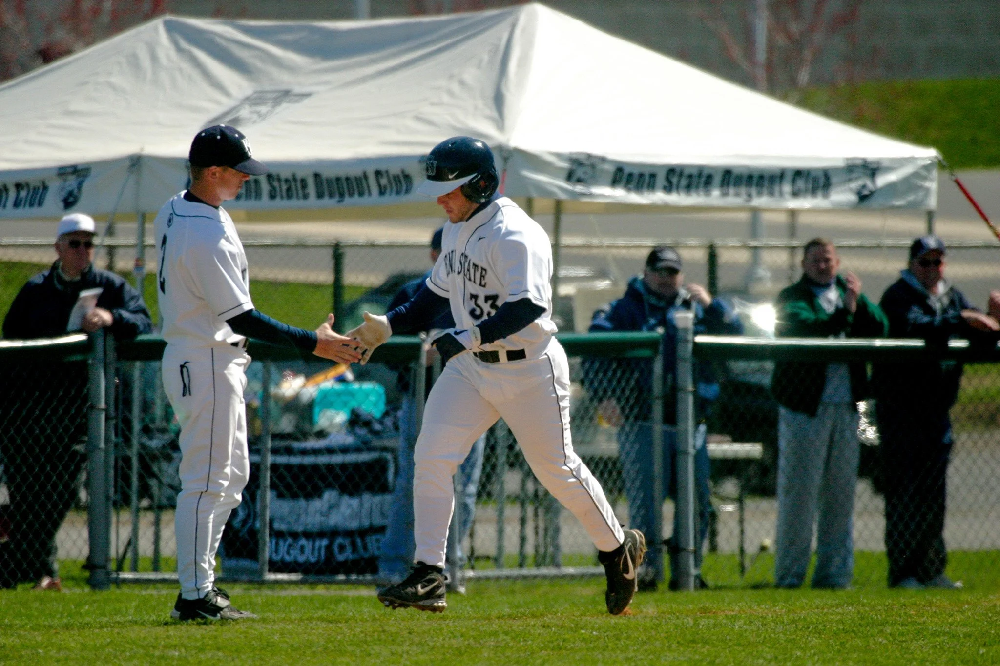 Two baseball players in white uniforms exchanging a high five on a baseball field during a game.