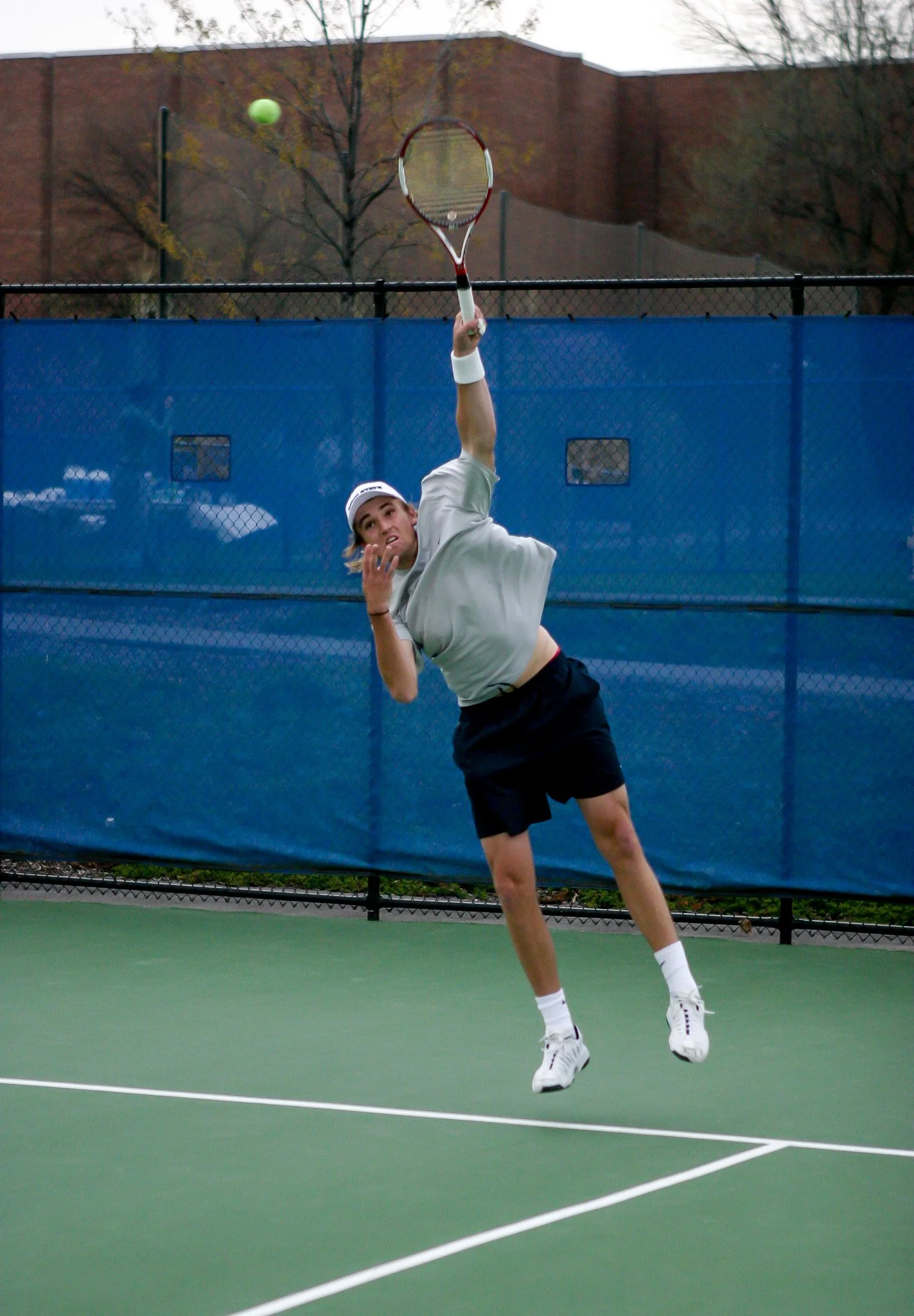 Young male tennis player leaping to hit a tennis ball with his racket on an outdoor court.