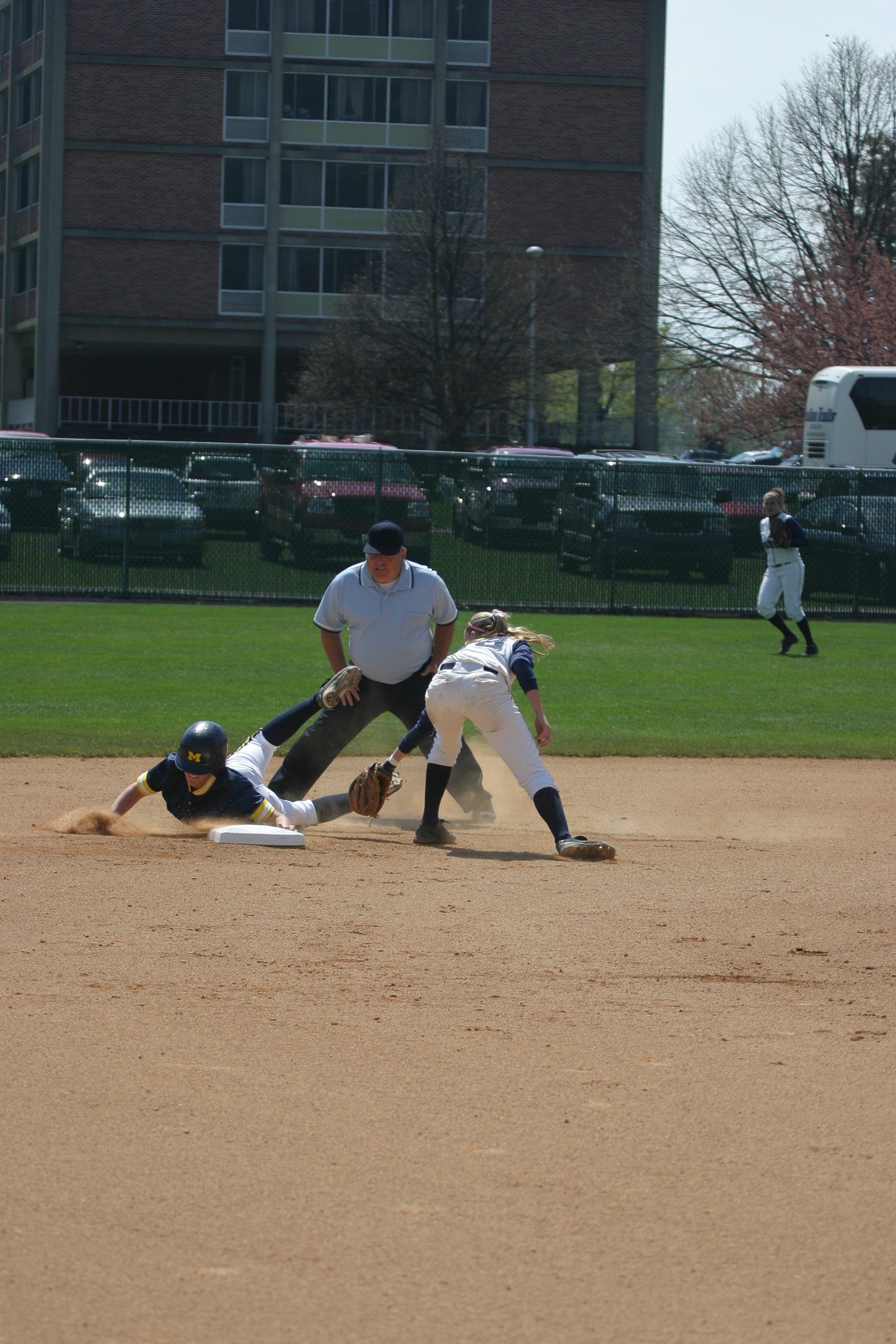 A baseball game with players, an umpire, and a coach on a field with a city background.