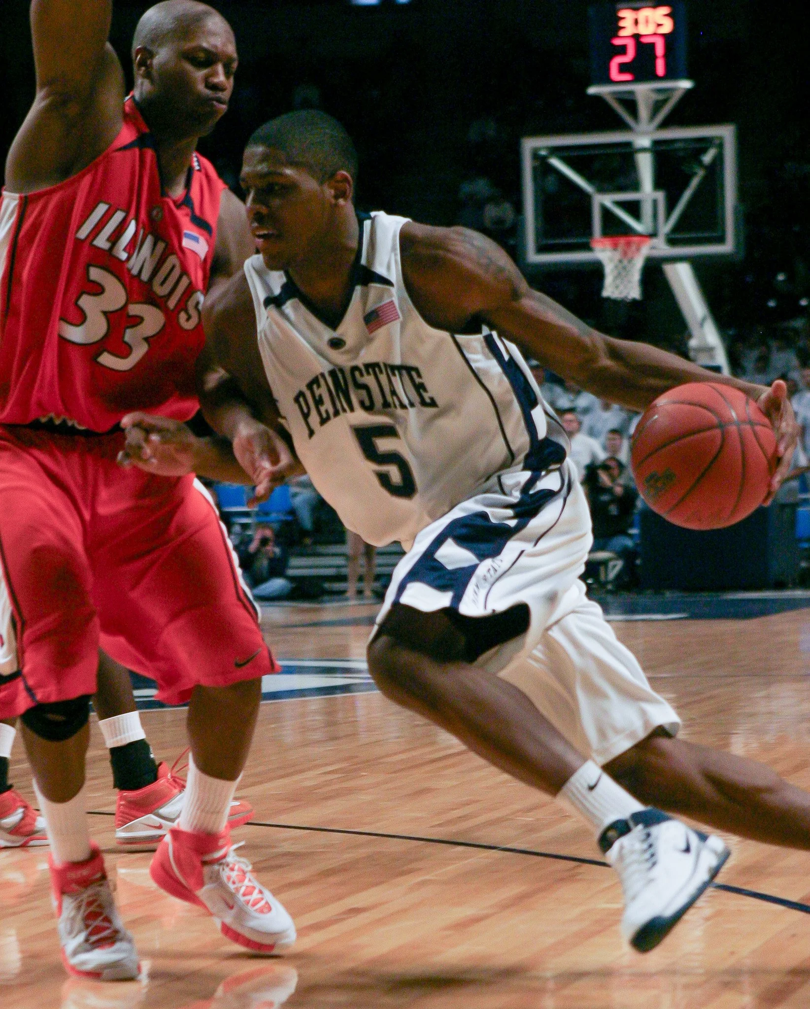Two basketball players from Penn State and Illinois competing for the ball during a game. The Penn State player is dribbling while the Illinois player is defending.