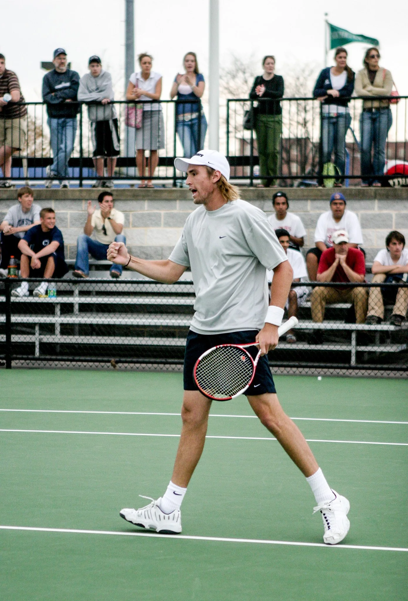 A man playing tennis on an outdoor court with spectators watching from the stands.