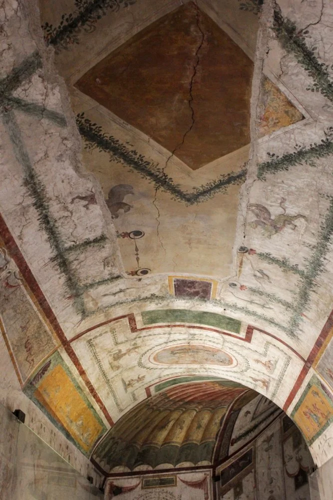 Frescoed ceiling with geometric designs, floral patterns, and clouds, showing signs of aging and wear.