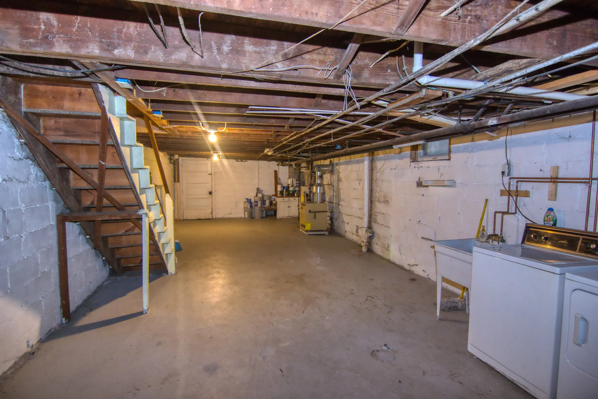 Basement with unfinished walls and ceiling, laundry area with washing machine and utility sink, concrete floor, and fluorescent lighting
