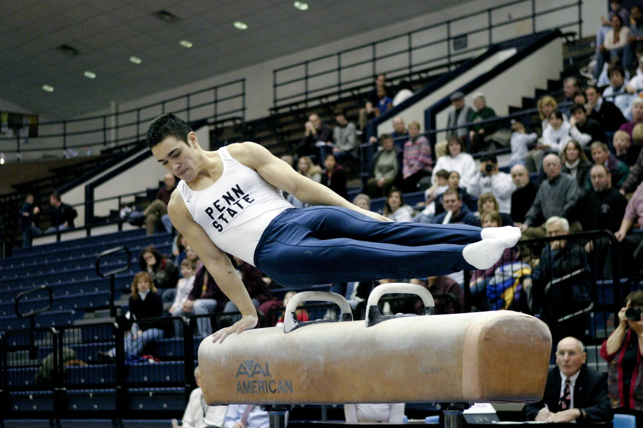 A male gymnast from Penn State performing a pommel horse routine during a gymnastics competition, with spectators watching in the background.