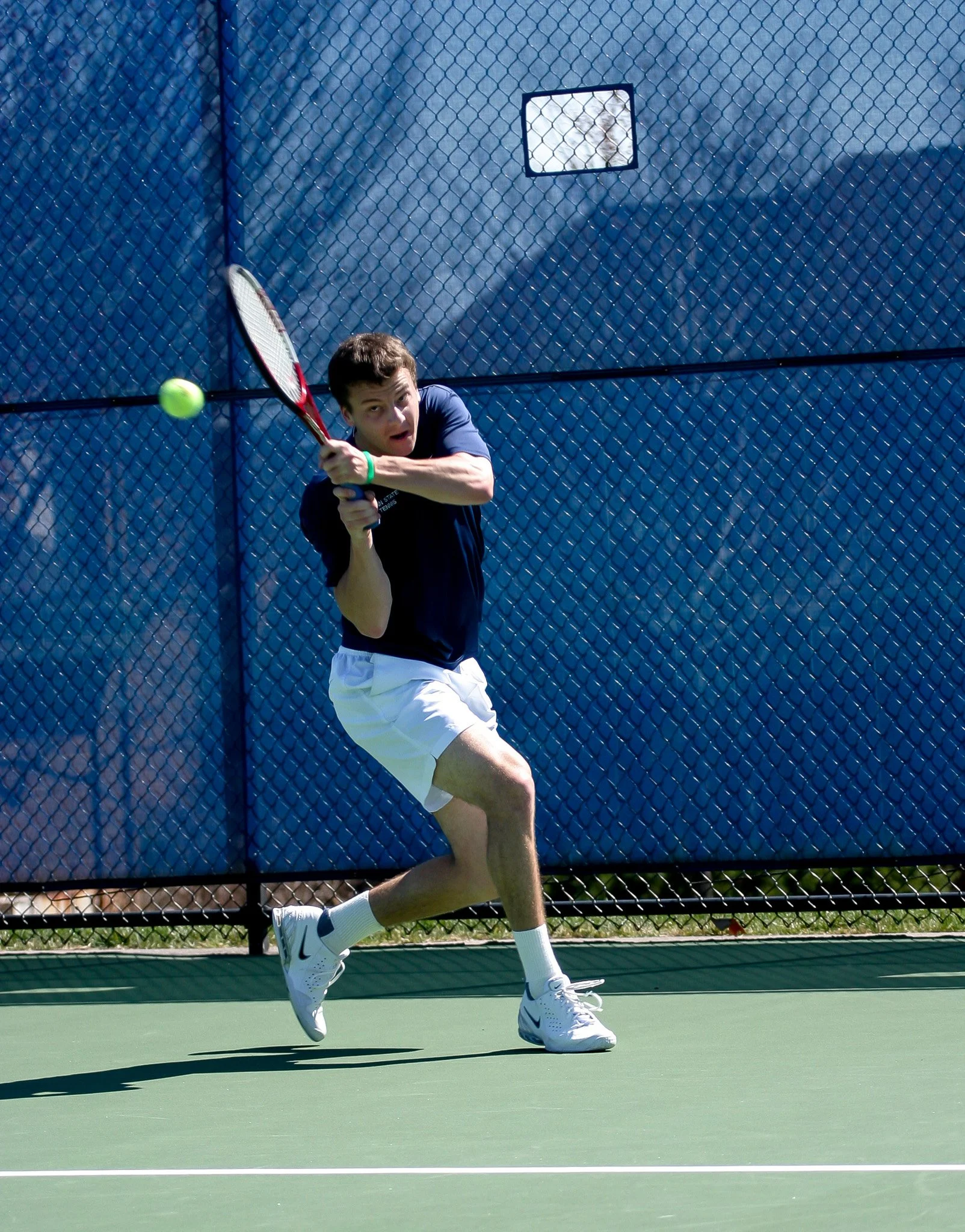 A young man is playing tennis on an outdoor court, preparing to hit a tennis ball with his racket.