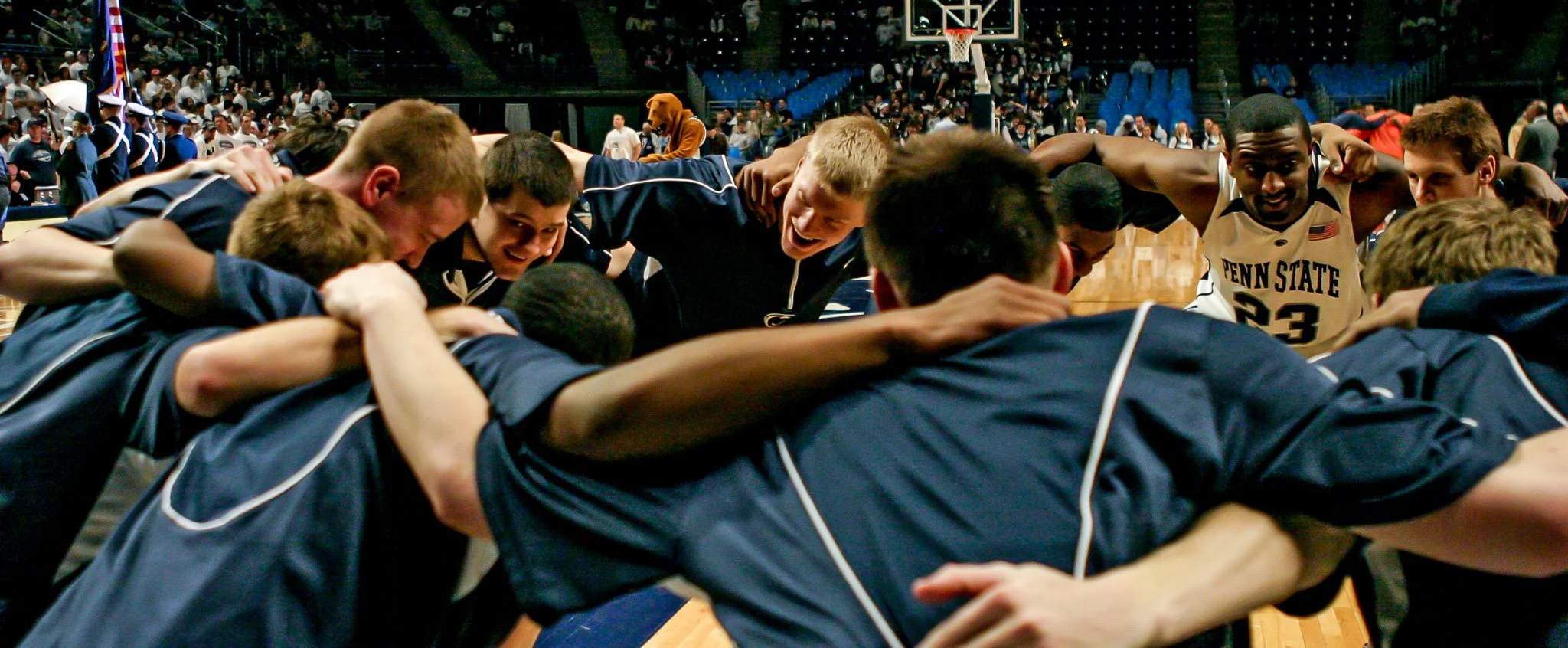 Penn State basketball team huddling and cheering on the court.