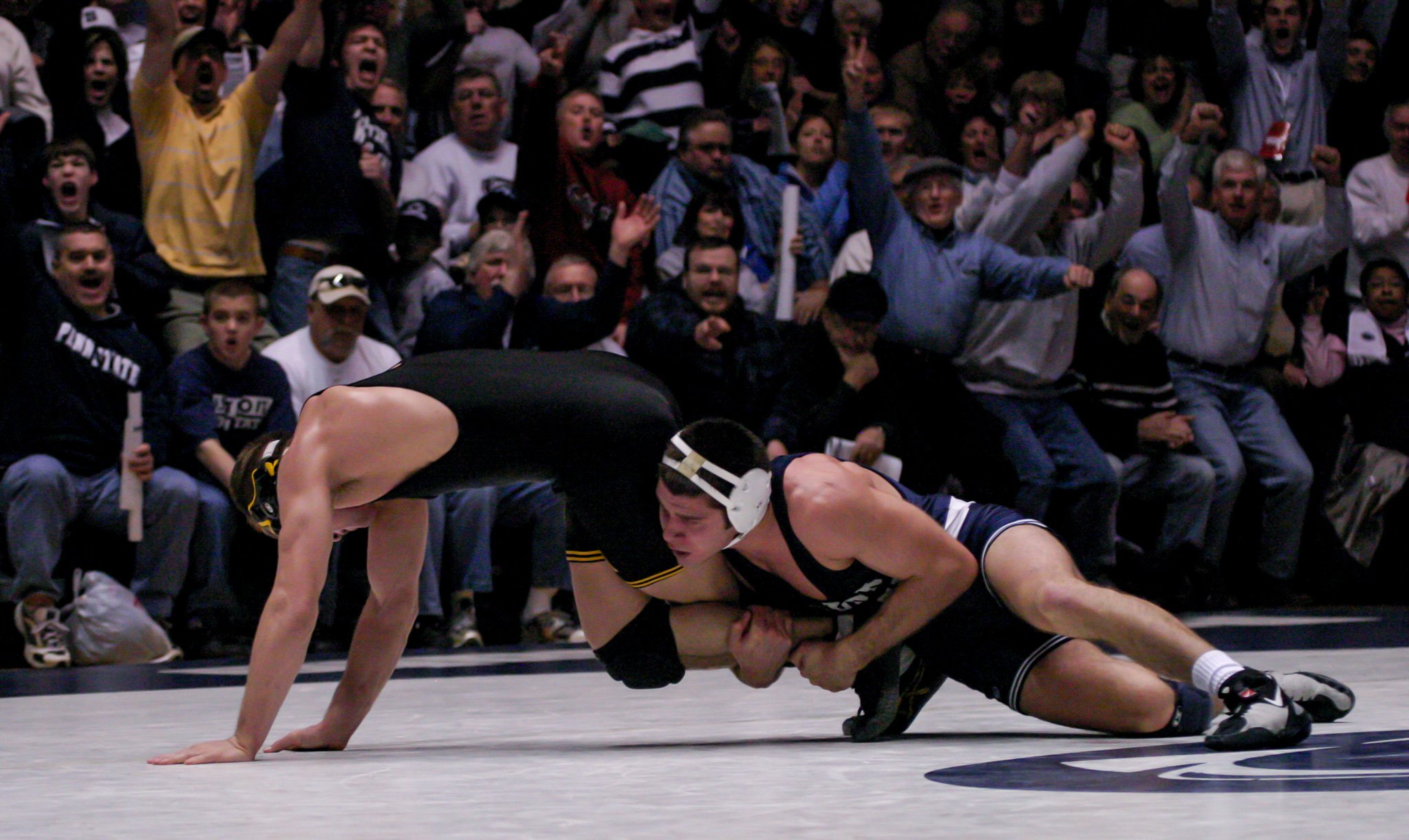 Wrestlers competing in a match on a wrestling mat with a cheering crowd in the background.