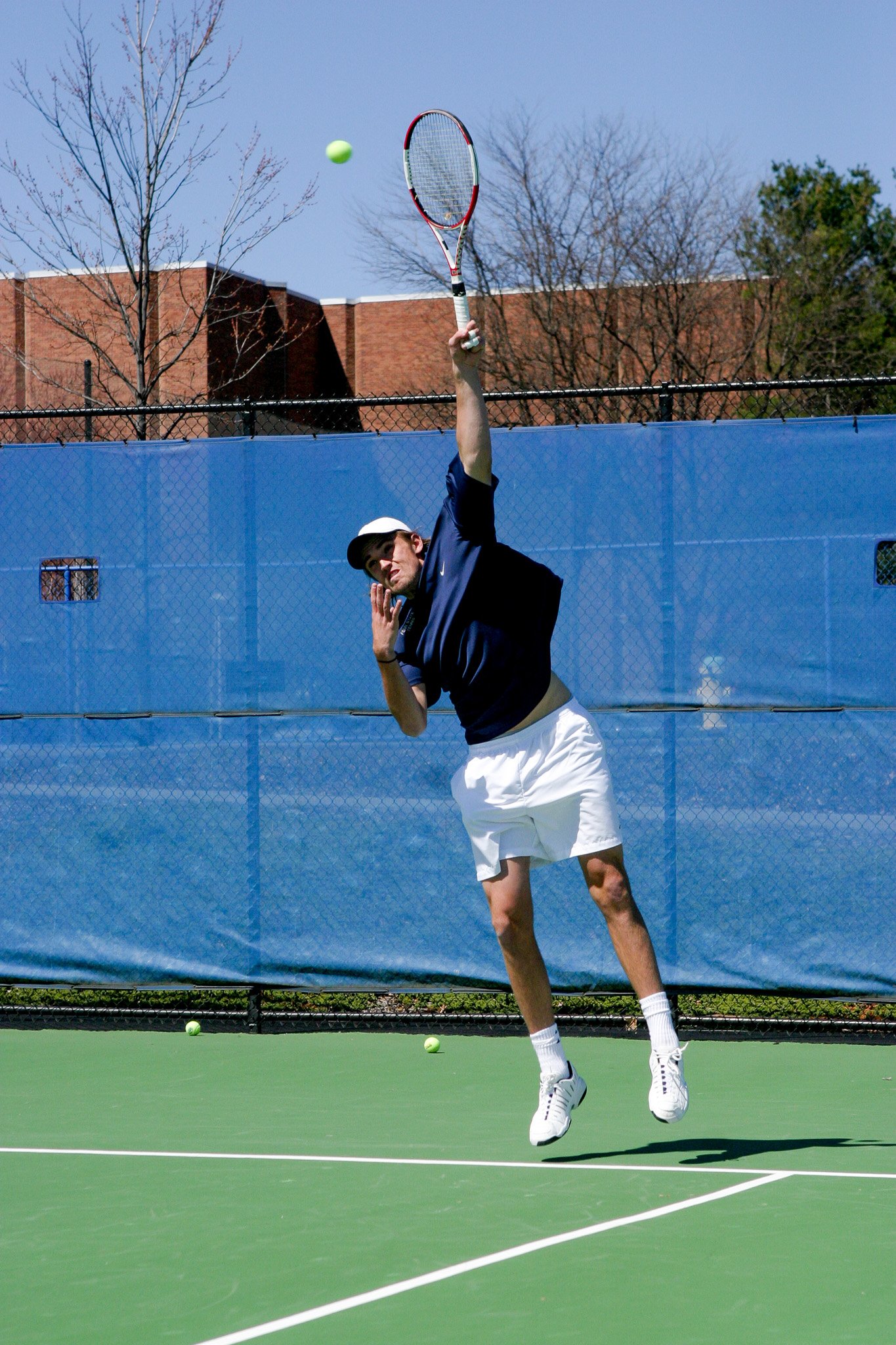 A man playing tennis on an outdoor court, jumping to hit a tennis ball with a racket.