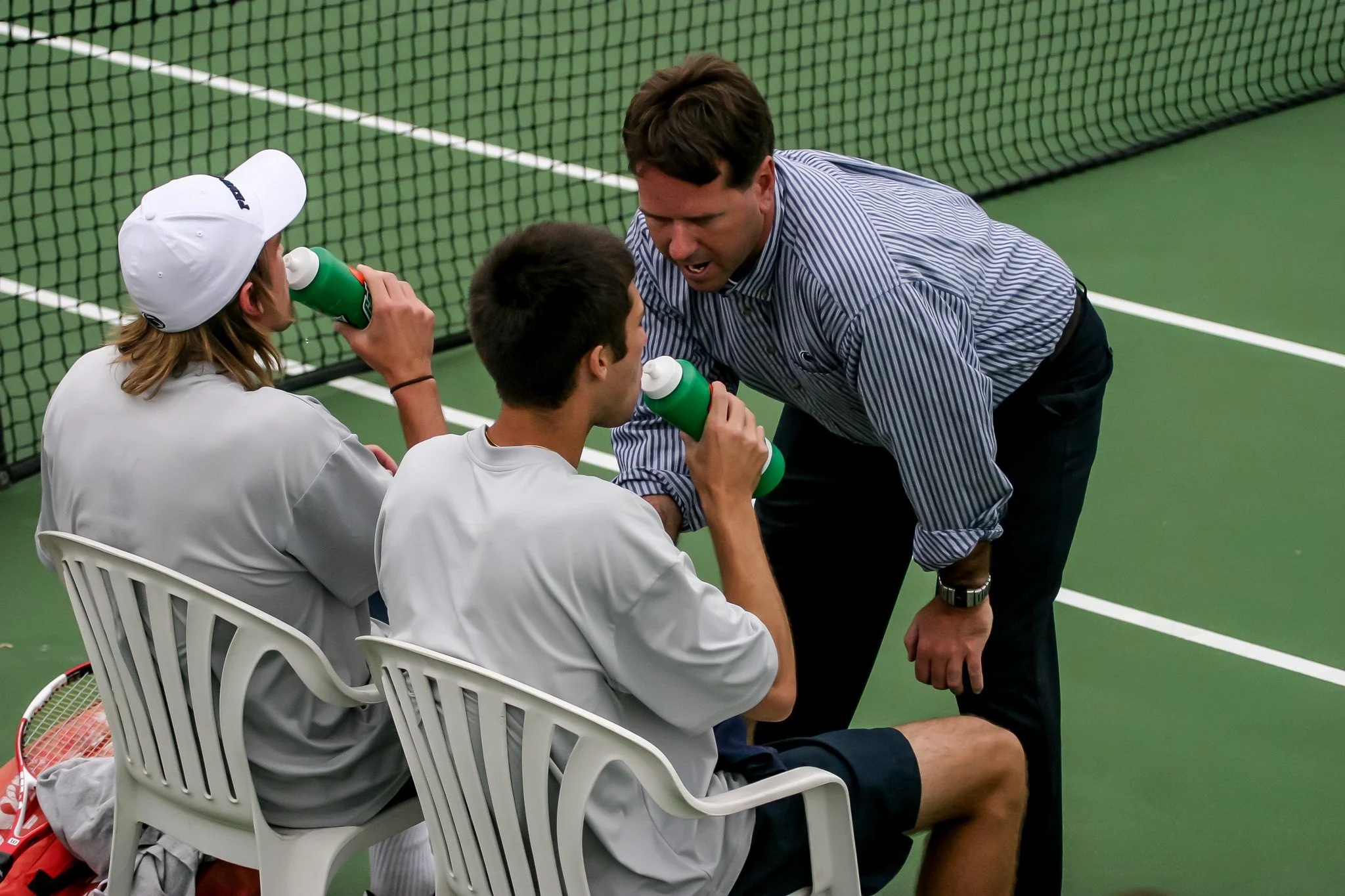A tennis coach arguing with two players during a break on the tennis court.