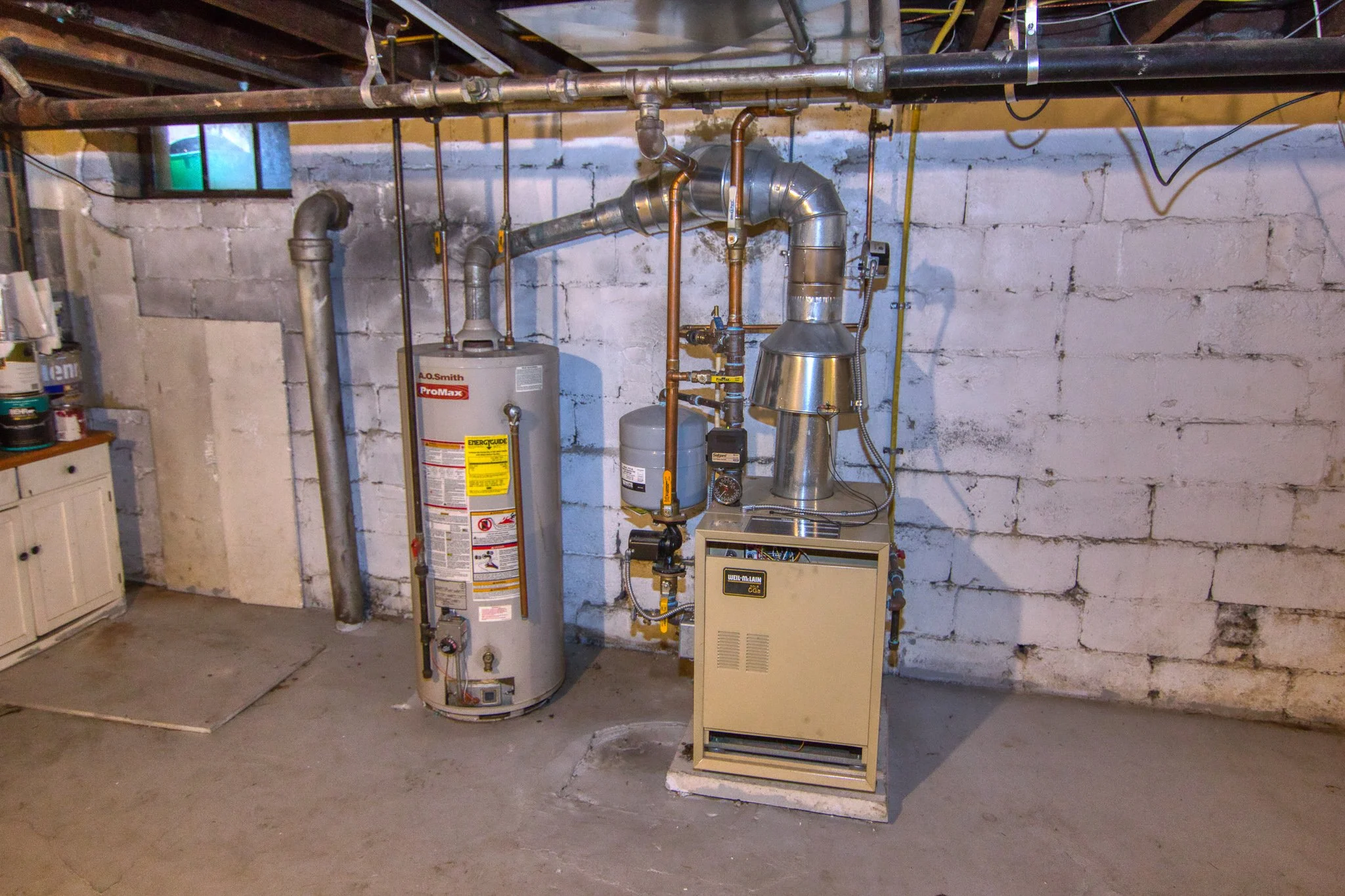 A basement utility room with a water heater and furnace connected to ductwork and pipes on a concrete floor.