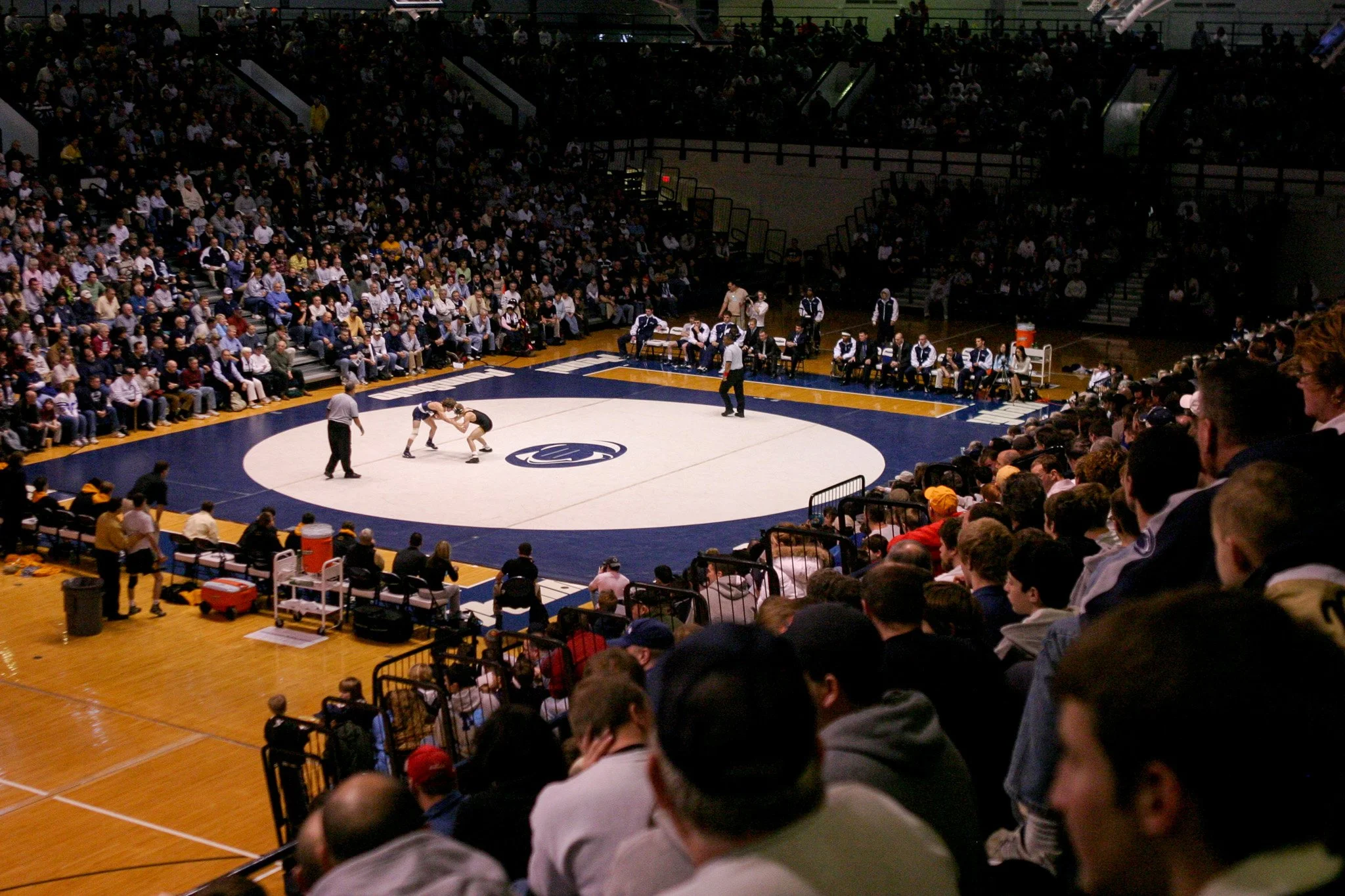 A wrestling match taking place in a large indoor arena, with an audience watching from all sides of the mat.