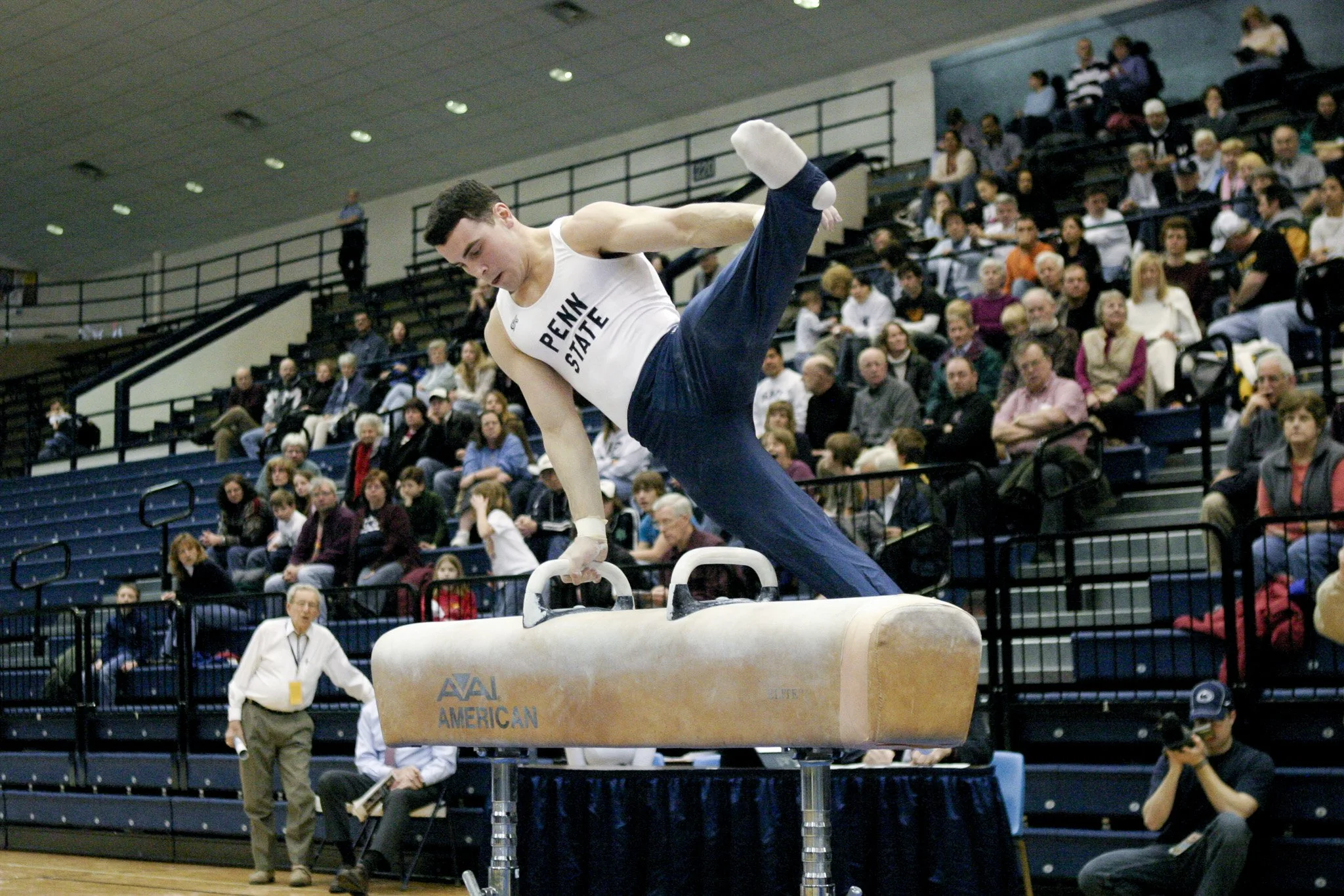 Male gymnast from Penn State performing on parallel bars during a competition, with crowd watching in the background.