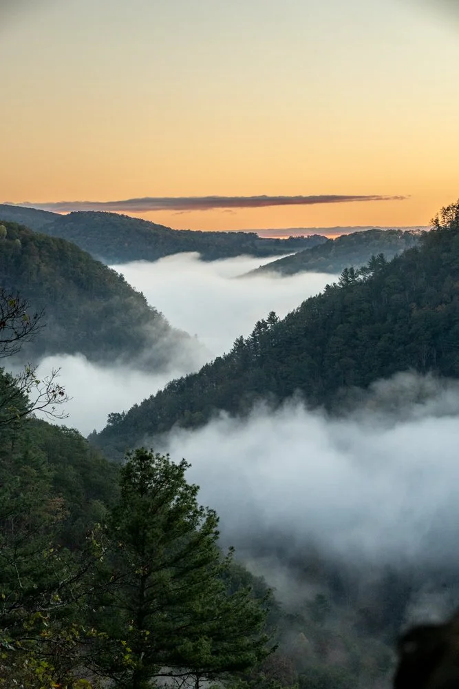 Morning fog rolling over green mountain hills at sunrise.