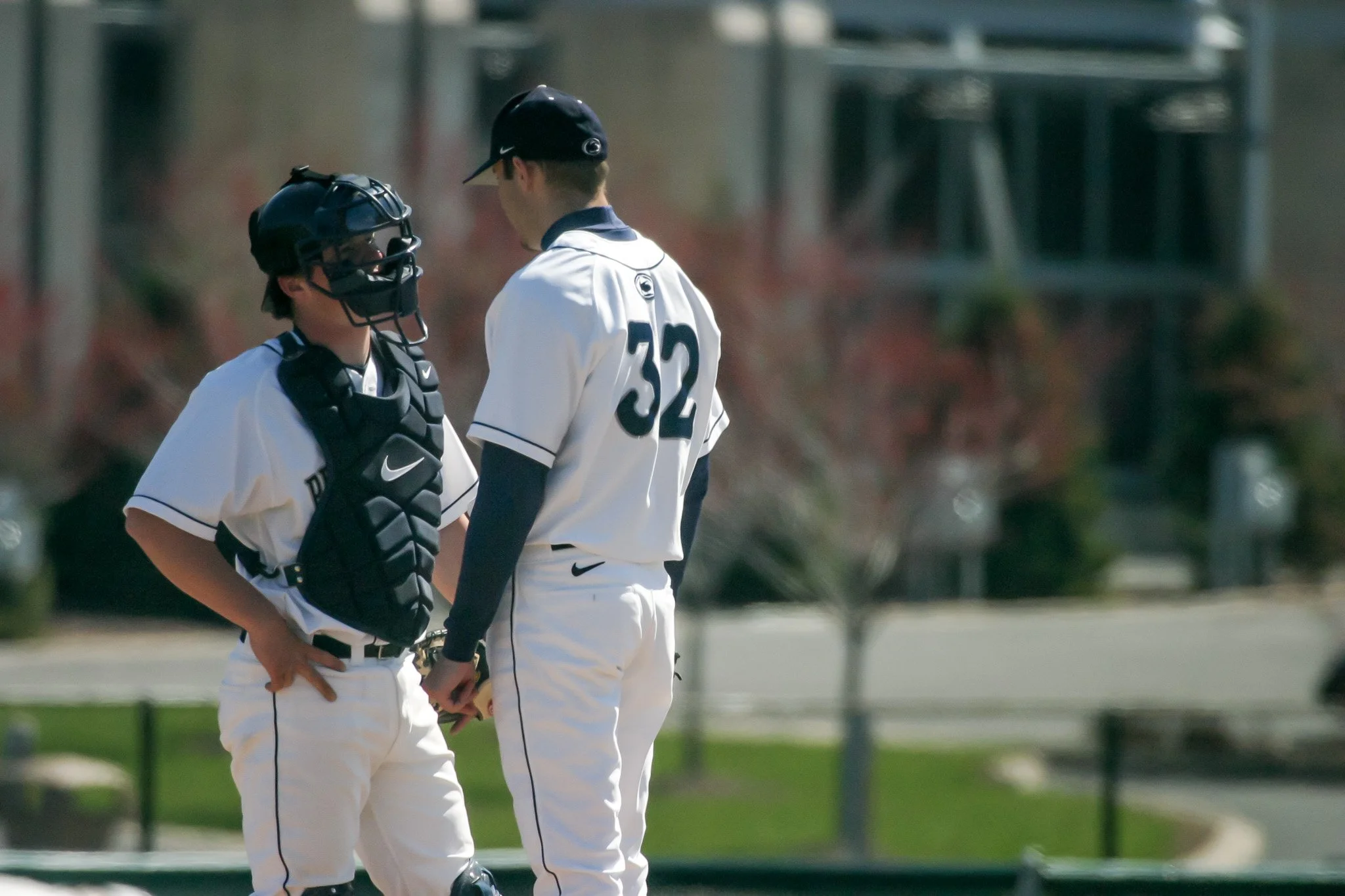 Two baseball players standing close, one wearing catcher's gear and the other with a baseball glove, in a conversation on the field.