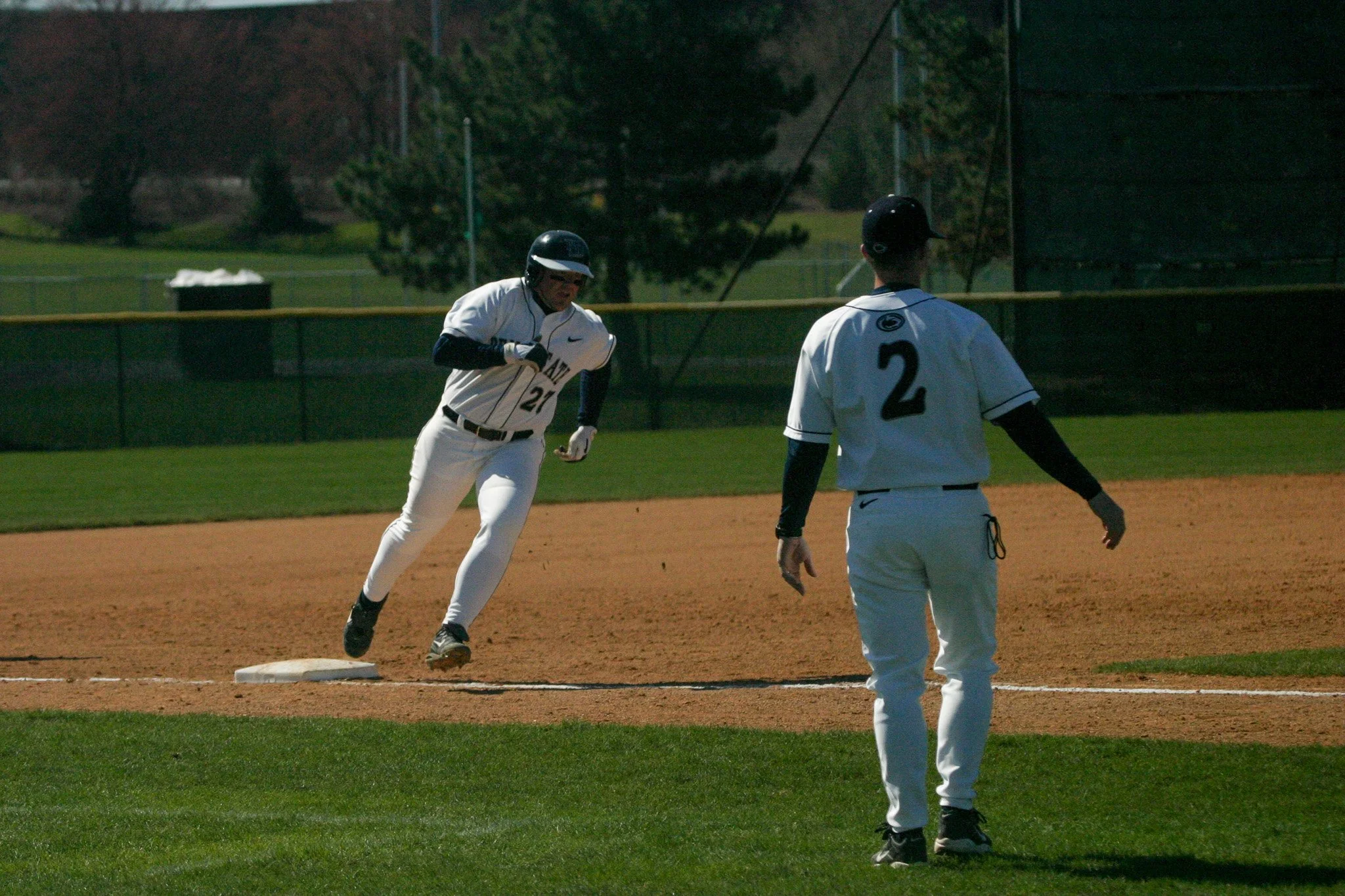 A baseball player wearing a white uniform with the number 21 is running towards a base, while another player in a white uniform with the number 2 stands nearby on the field.