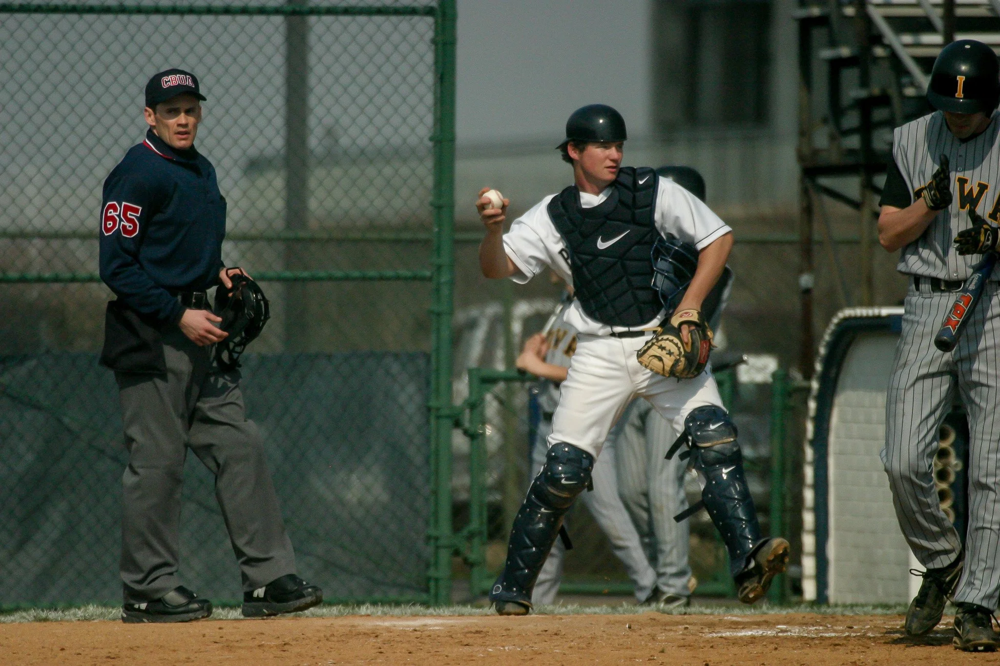 A baseball player in a black helmet and protective gear, with a glove and ball, is running towards first base during a game.