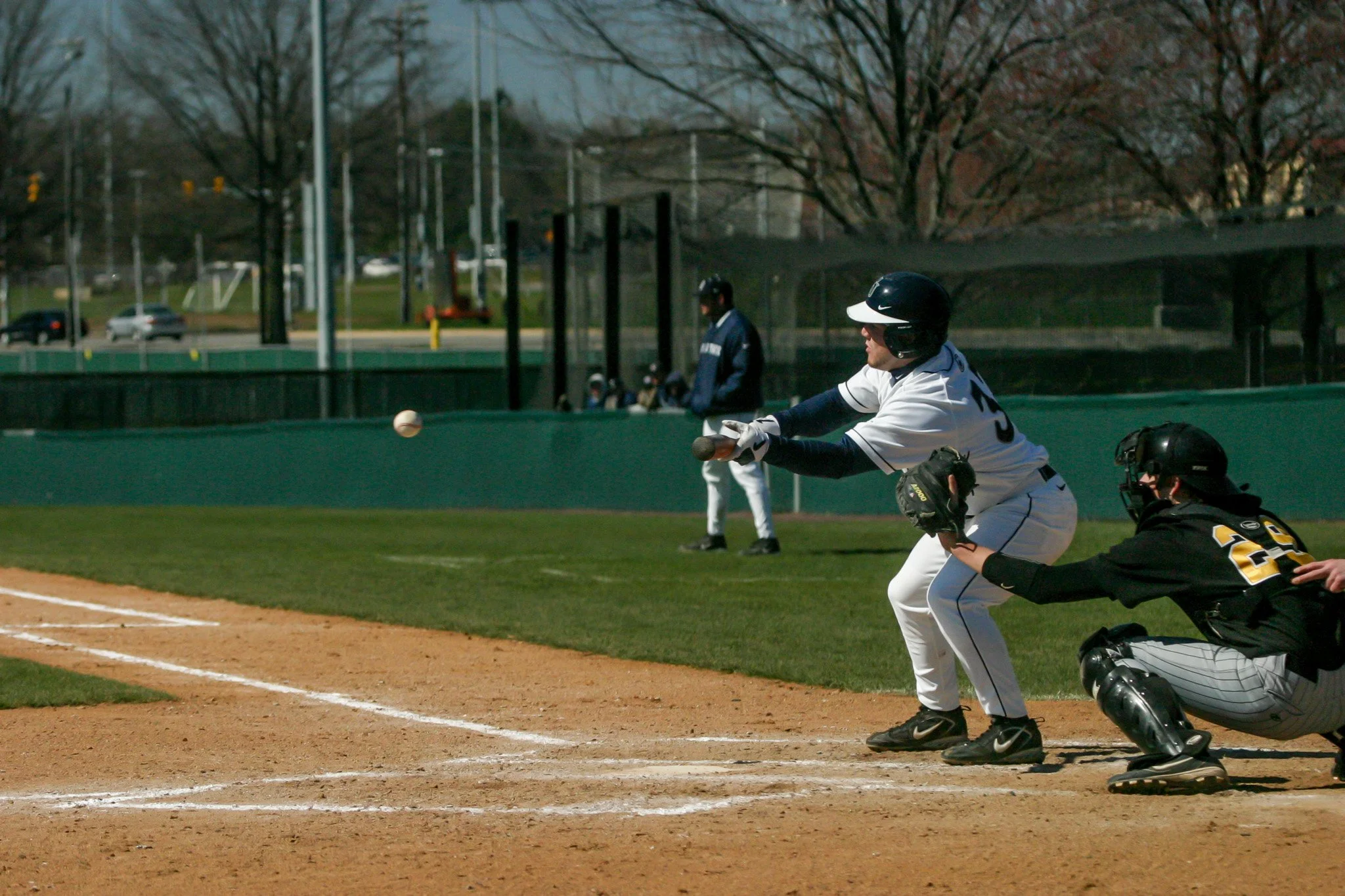 A baseball player in white uniform and black helmet hitting a pitched ball at home plate during a game.