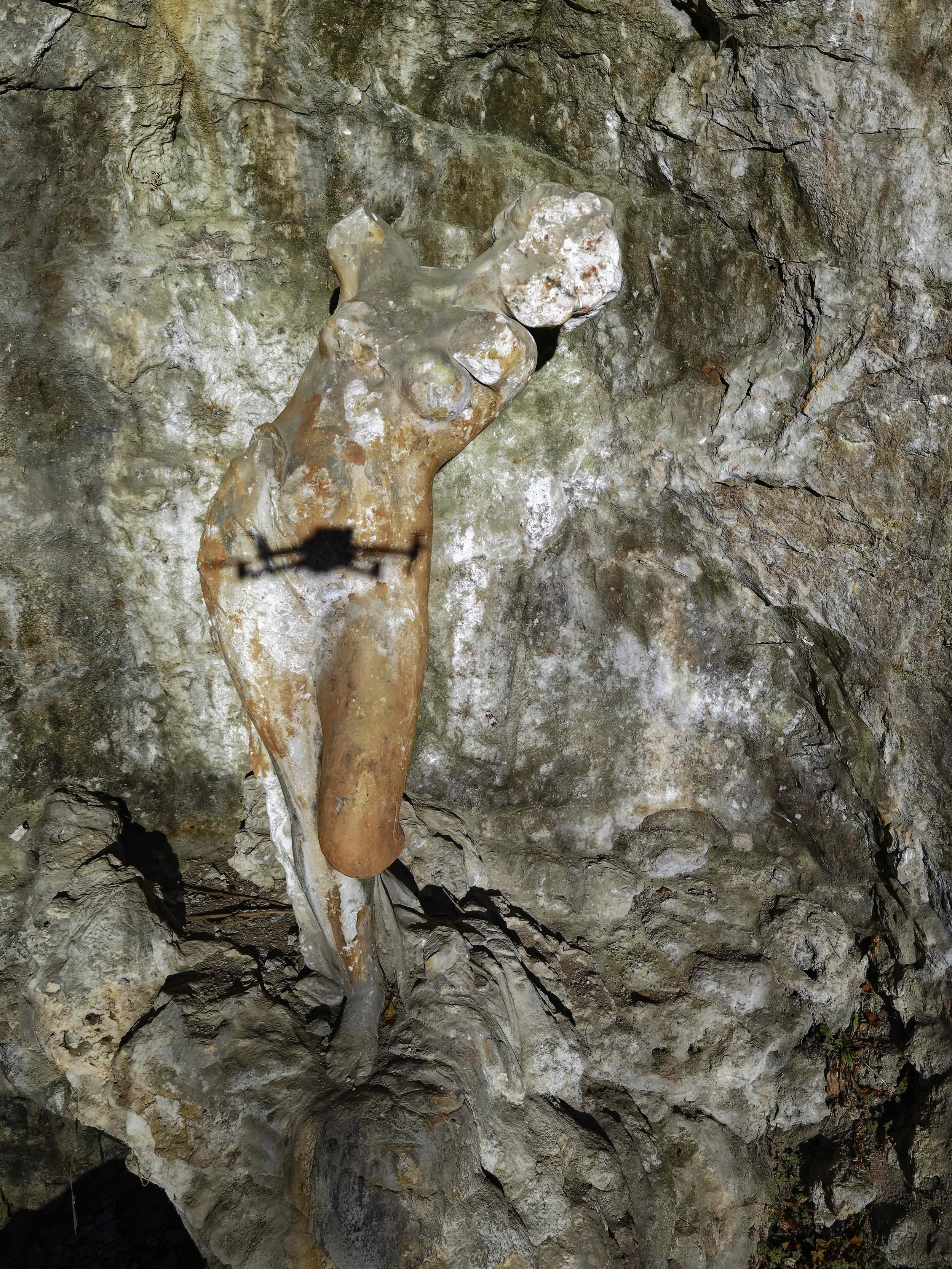 Eine Skulptur einer menschlichen Figur, die an einer Felswand angebracht ist, in einer Höhle oder einem Felsaggregat.