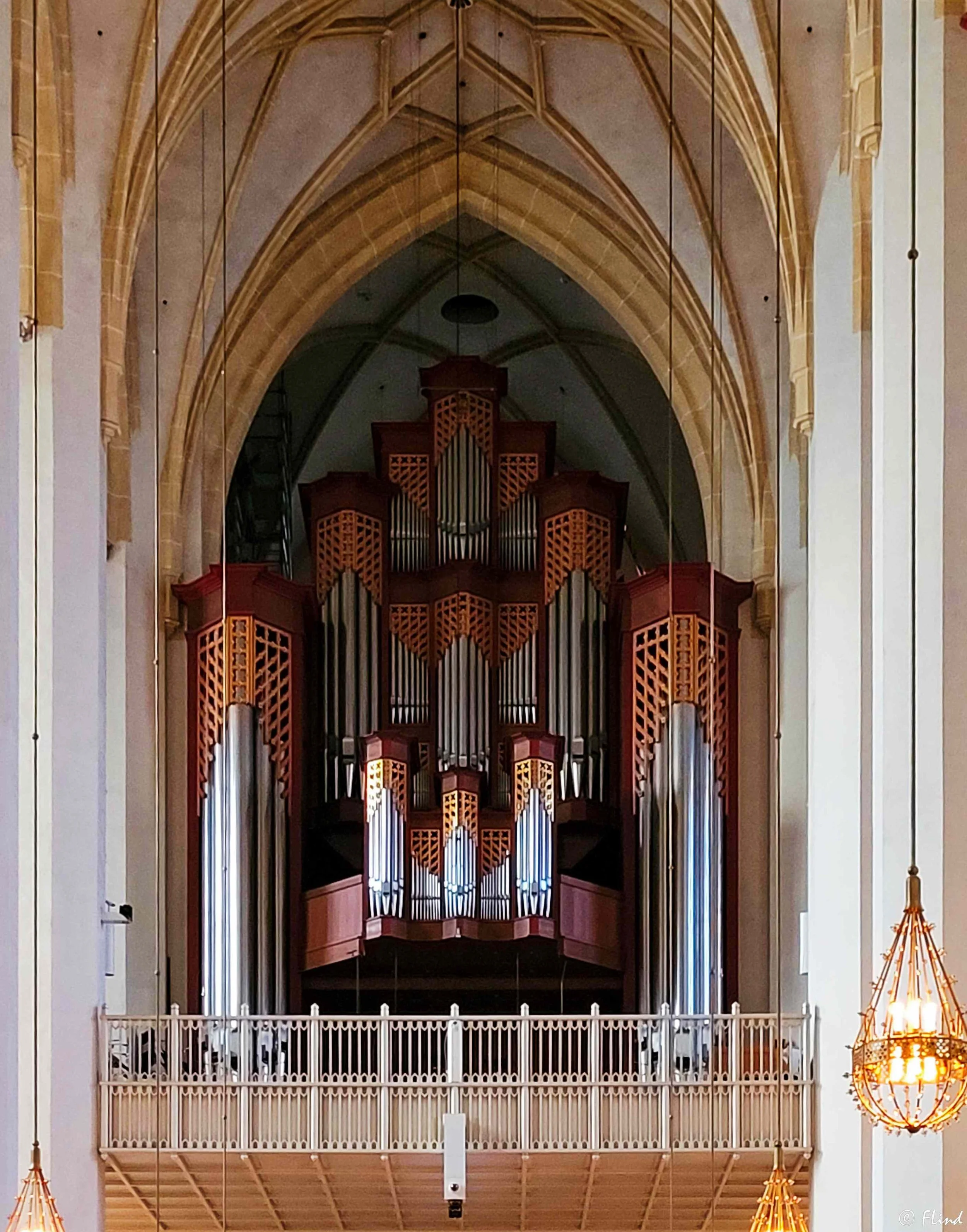 Ein großes Kirchen- oder Konzertsaal-Orgel mit Holzgehäuse und Metallpfeifen im Altarraum, umgeben von hohen, gewölbten Steinbögen und mit einem Balustraden im Vordergrund.