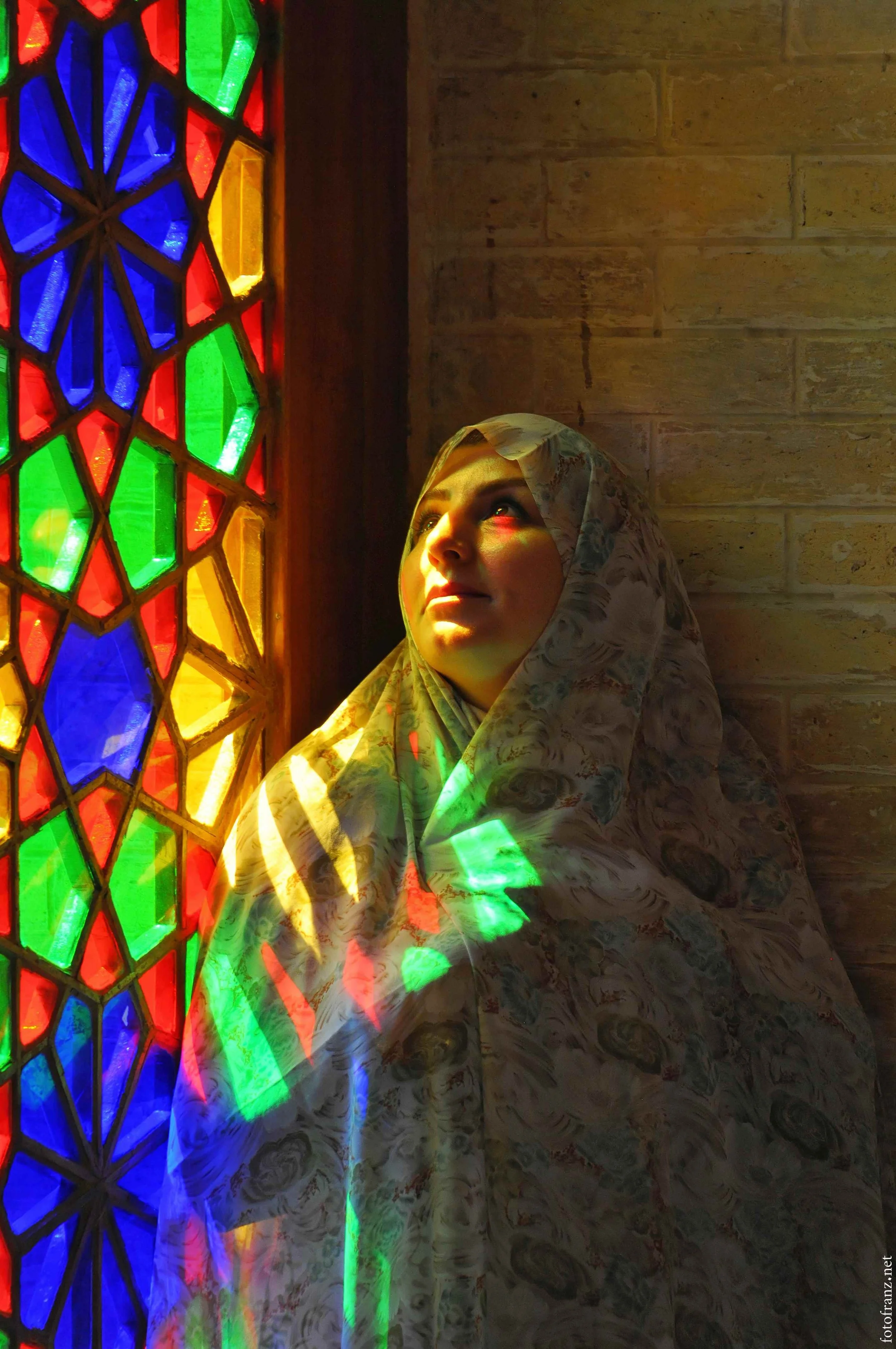 Frau mit Schleier blickt zur bunten, bemalten Fenster, durch das Licht einfällt.