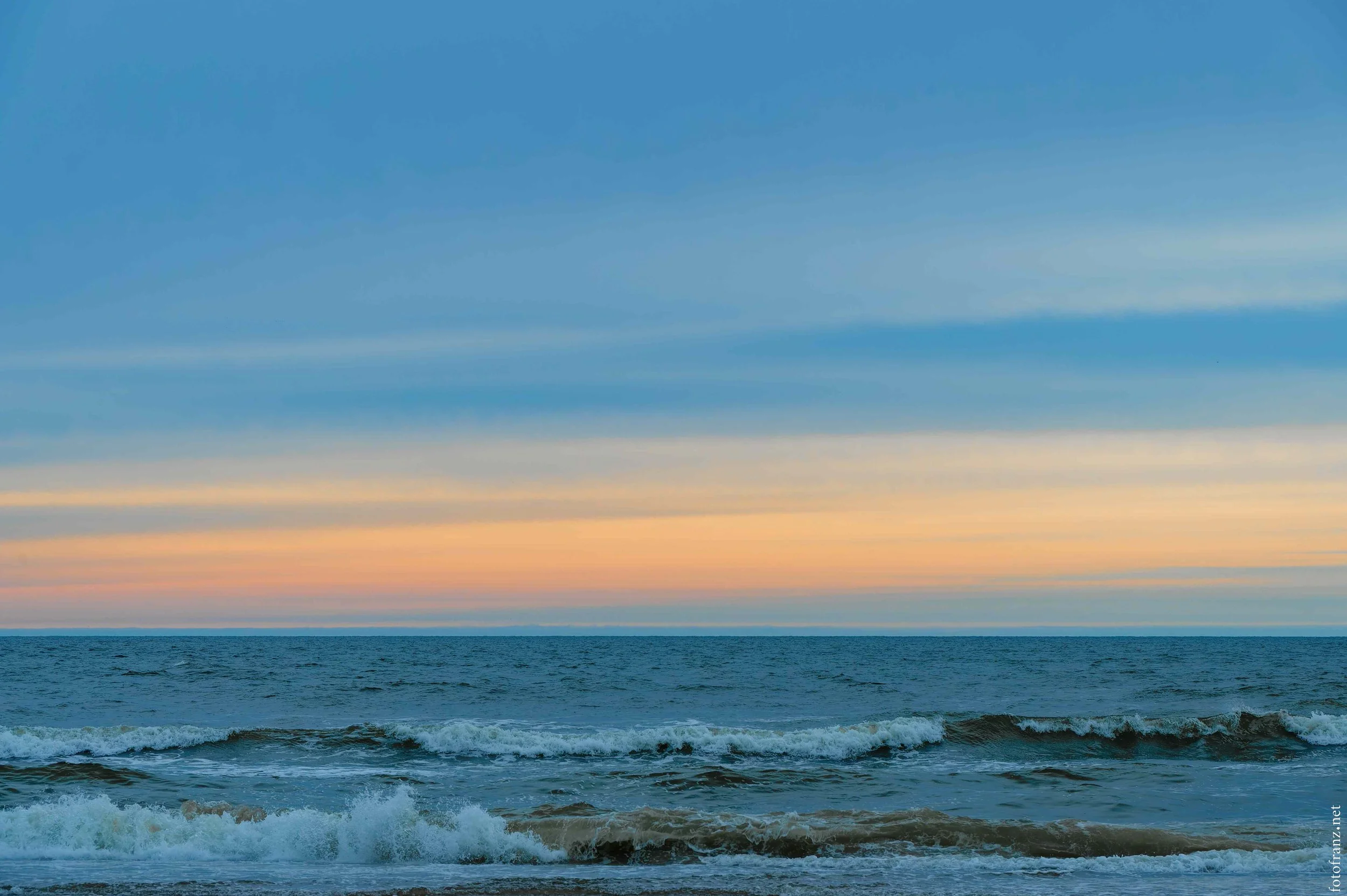 Ein Meer mit kleinen Wellen und ein Himmel mit Pastellfarben beim Sonnenuntergang