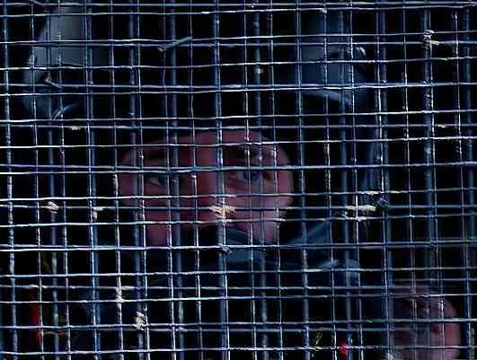 Junge, der durch ein Metallgitter blickt.