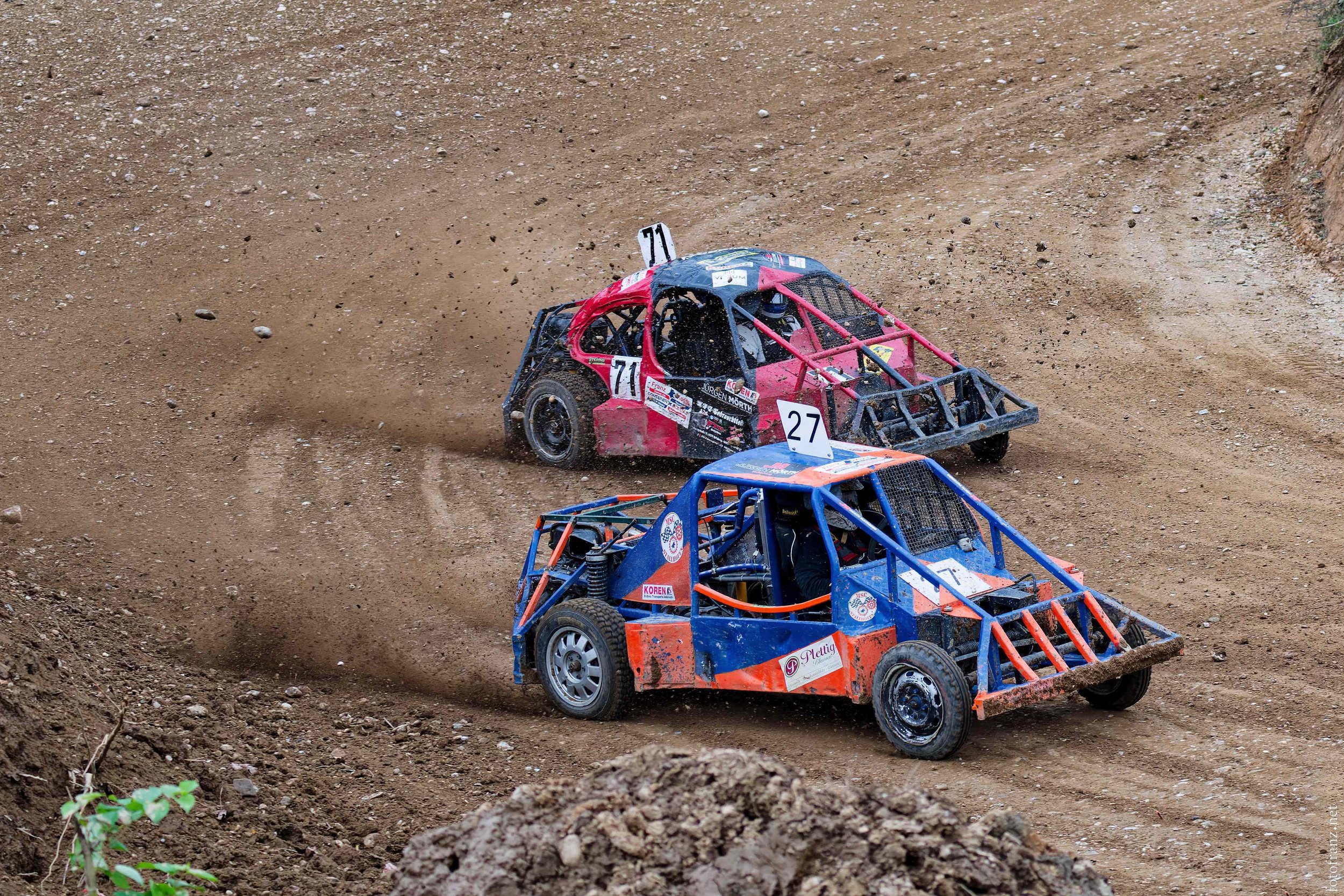 Zwei Offroad-Rennwagen fahren auf einer staubigen Wettkampfstrecke.