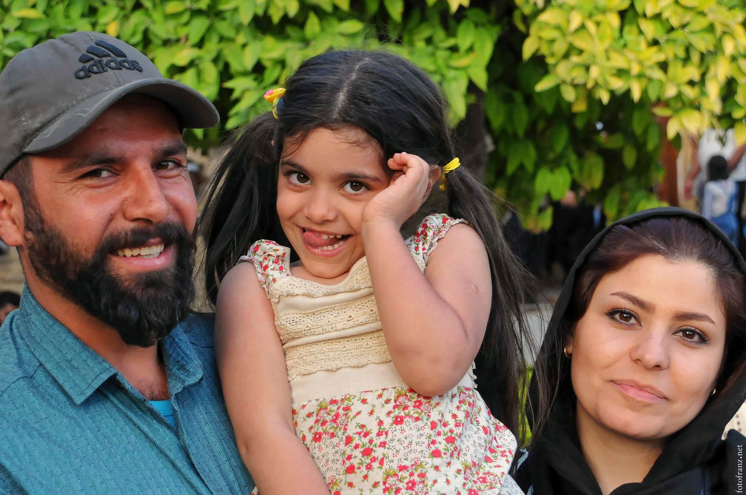 Eine Familie mit einem Mann, einer jungen Frau und einem Mädchen, die im Freien vor einem Baum stehen.