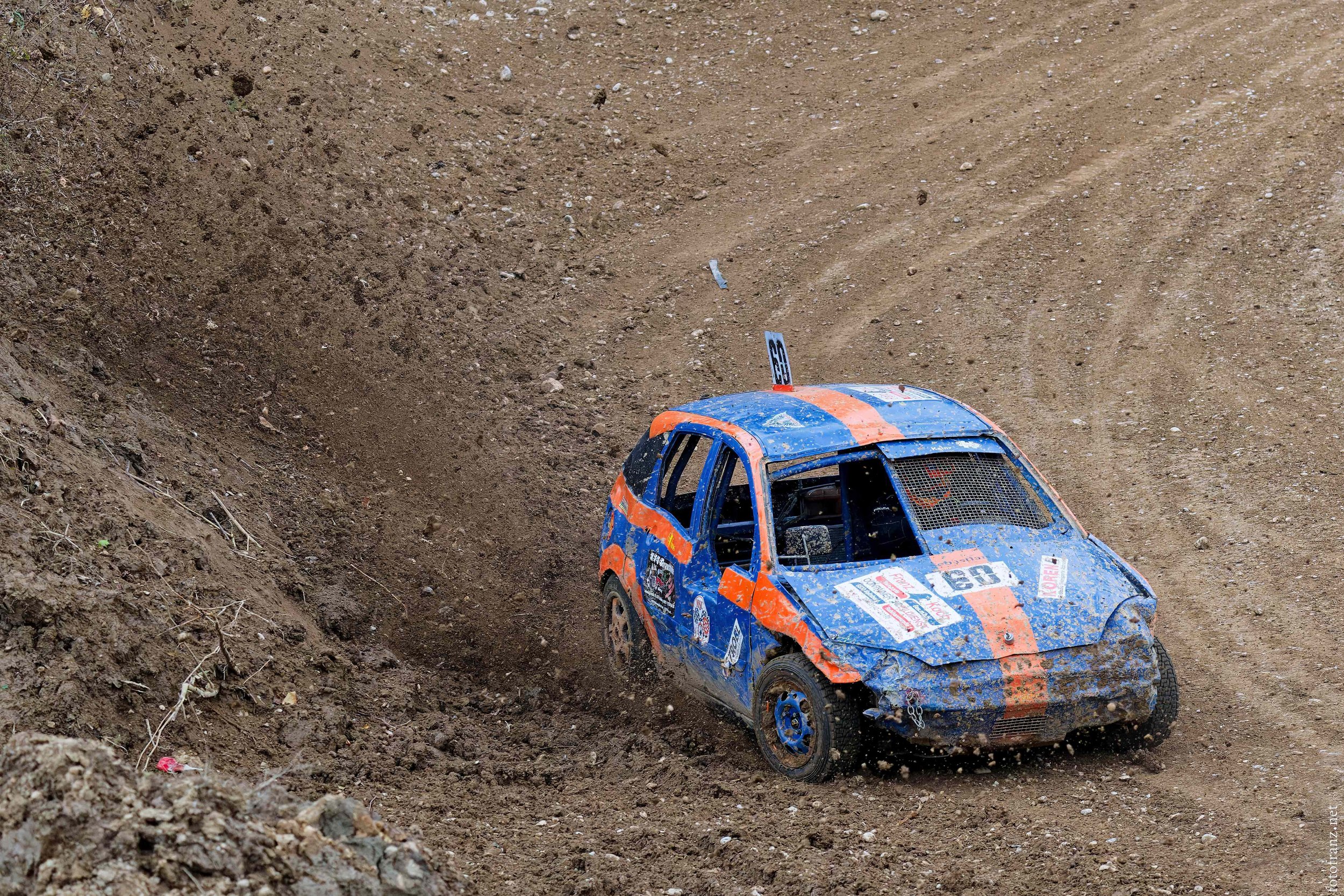 Ein verunglückter kleiner Rennwagen, der auf einem schlammigen Offroad-Strecke liegt.