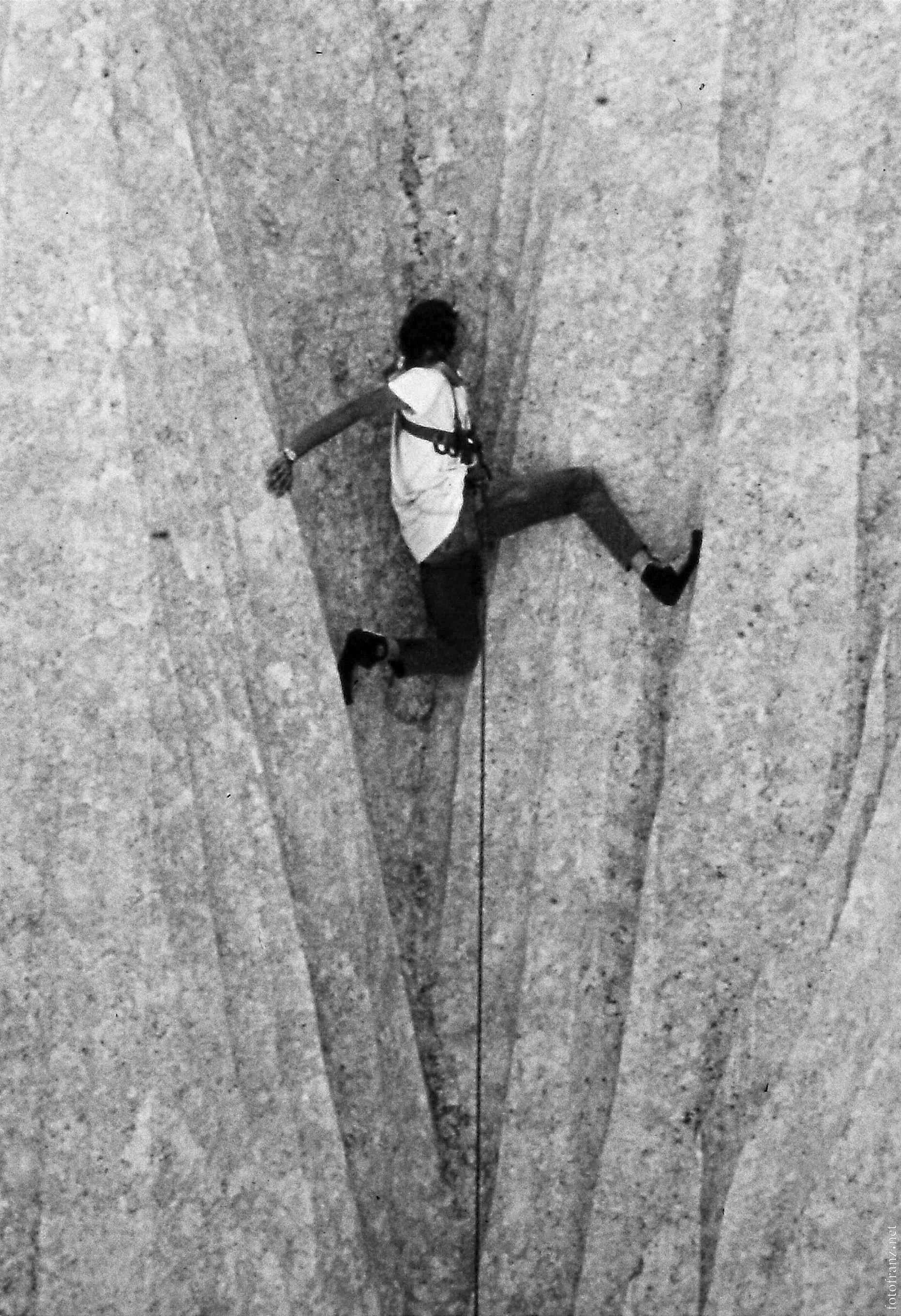 Mensch beim Klettern an einer vertikalen Steinmauer, getragen mit Kletterausrüstung.