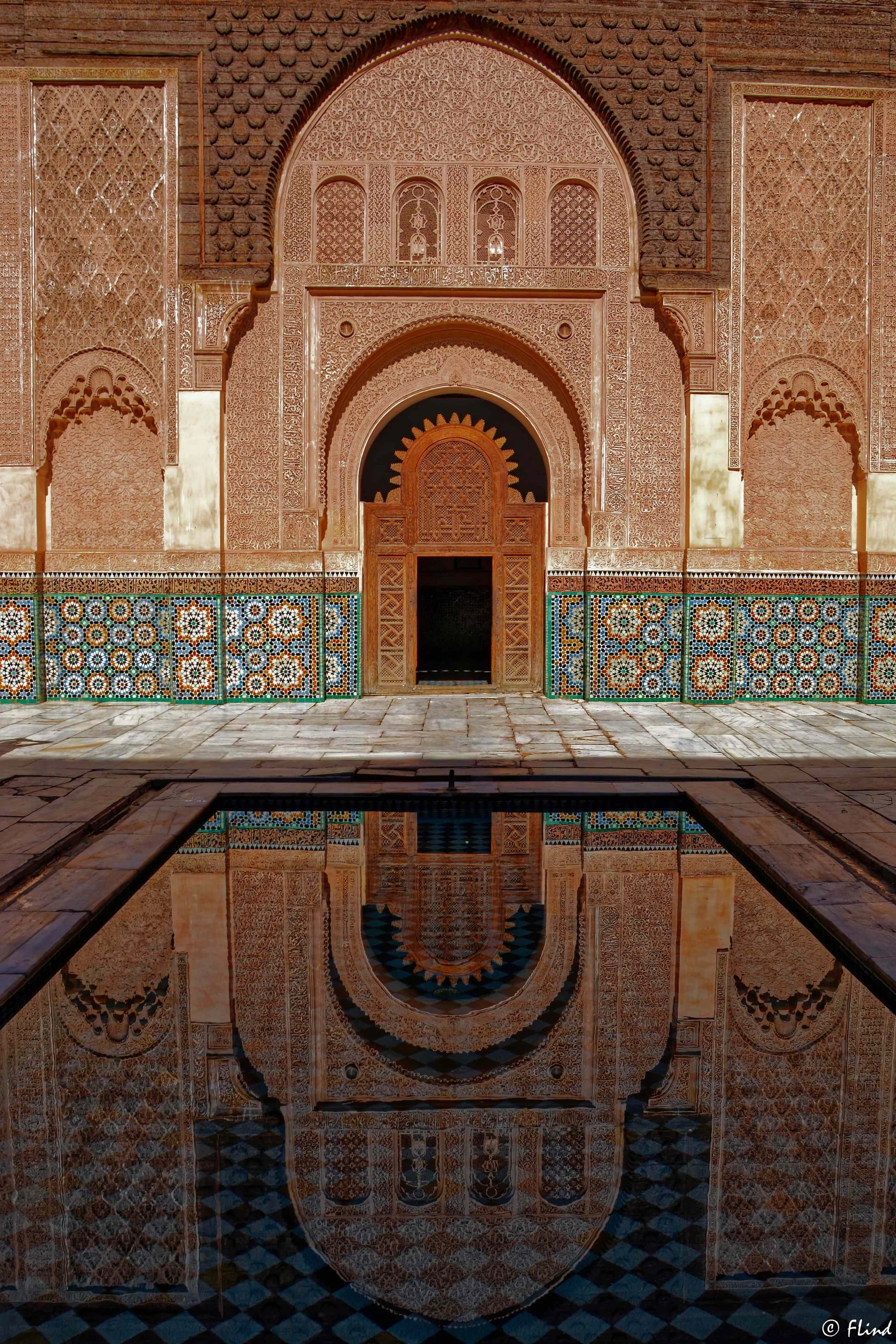Innenansicht eines maurischen Palastes mit detaillierten Wandverzierungen, bunten Mosaikfliesen und einem stilvollen Wasserbecken, das die Architektur spiegelt.