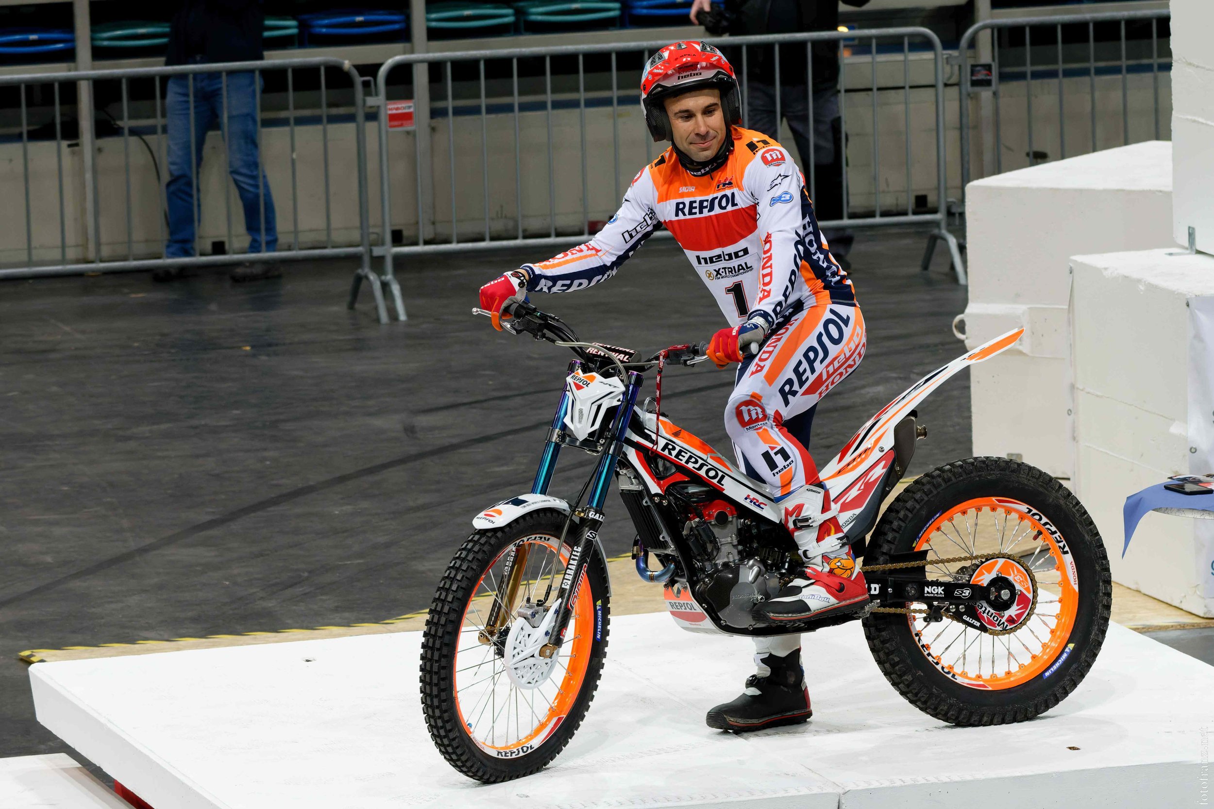 Motorsportler in Repsol Honda Team Kleidung auf einem Motorrad mit orange und weißem Design auf einer Plattform, vermutlich nach einem Rennen.