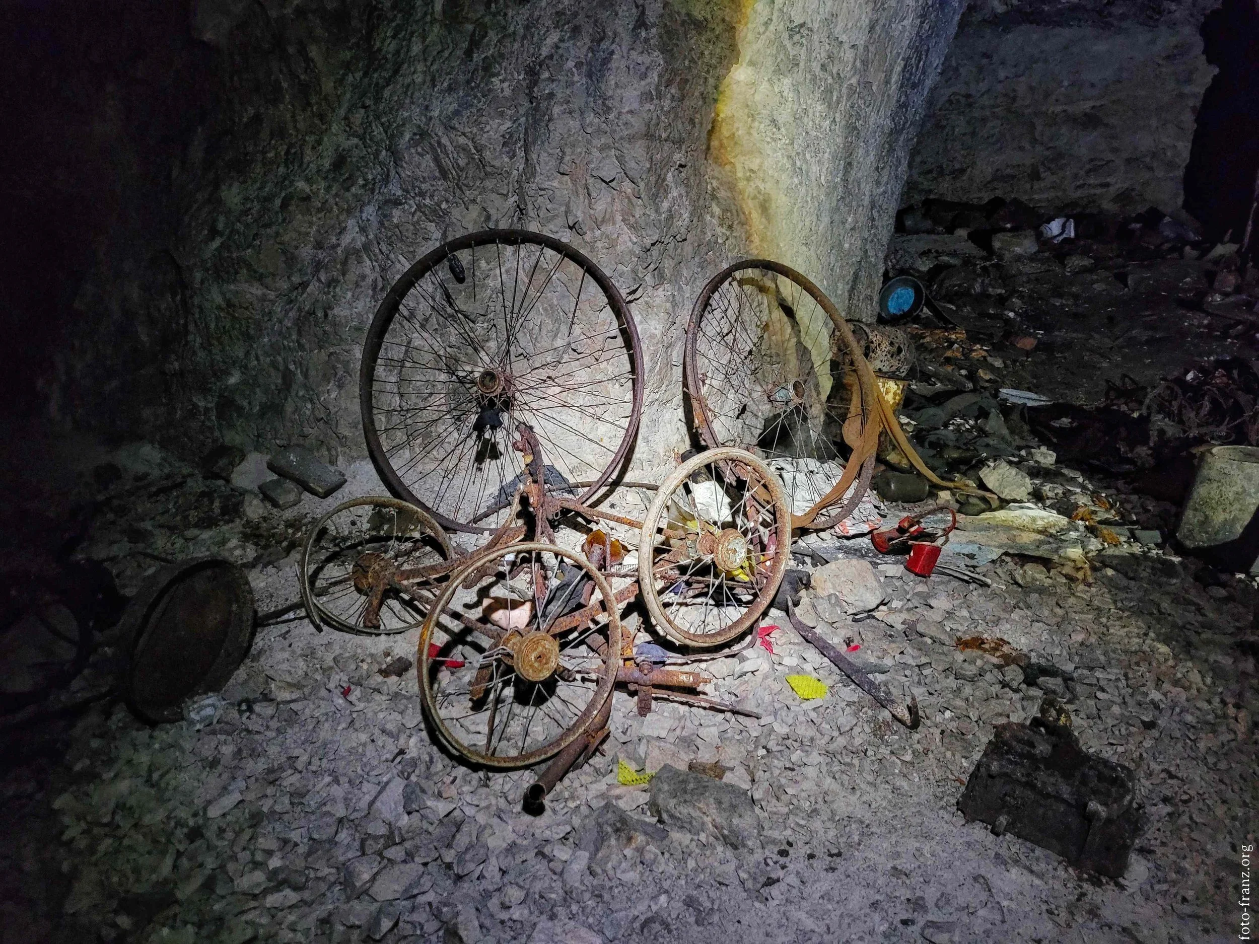 Verschmutzte, verrostete alte Fahrräder und Fahrradteile auf einem Steinboden in einer Höhle oder einem Tunnel.