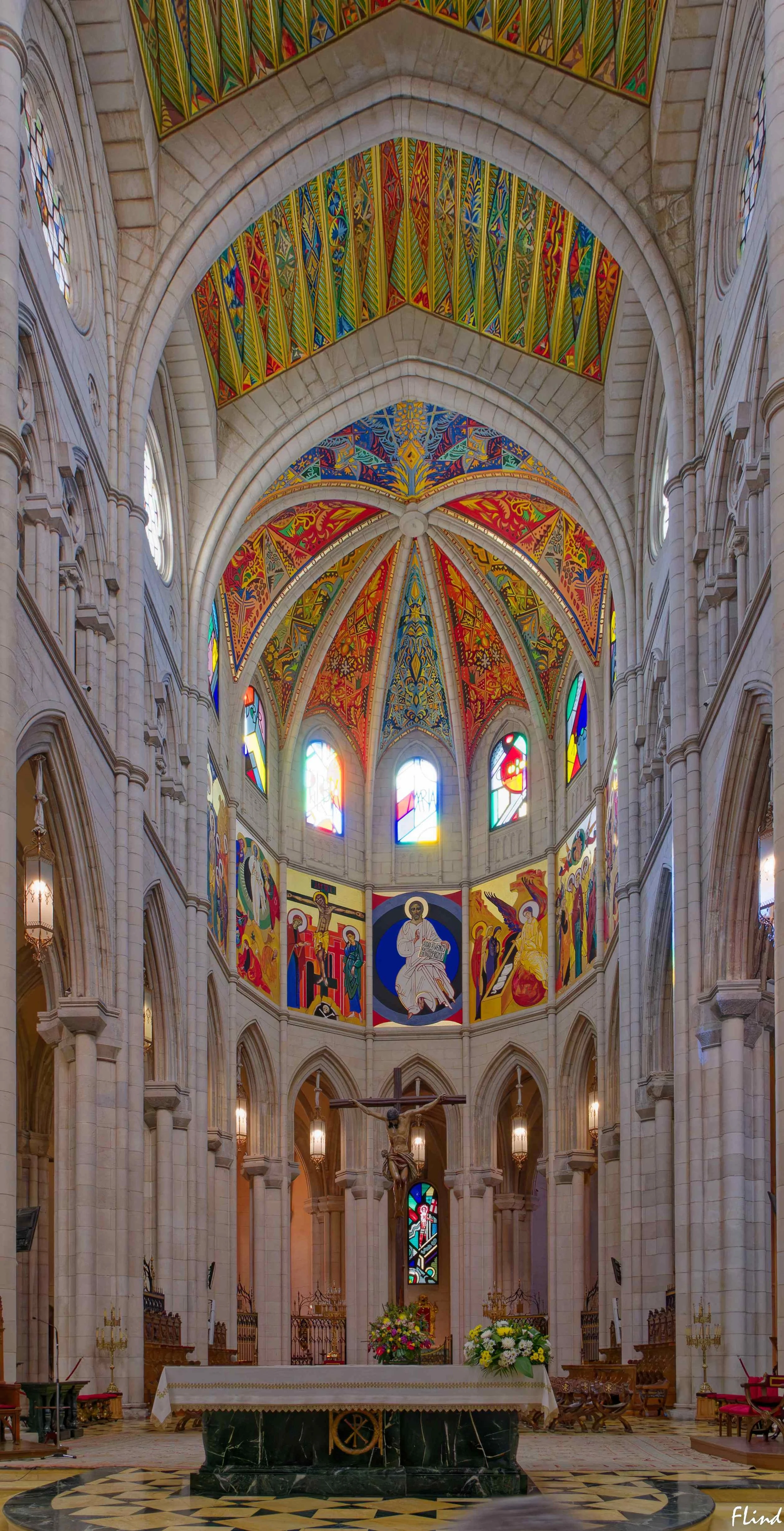 Innenansicht einer gotischen Kirche mit prachtvollem farbig verziertem Decke und Altar, eines Kreuzes mit Jesus Christus, bunten Fenstern und religiösen Wandbildern.
